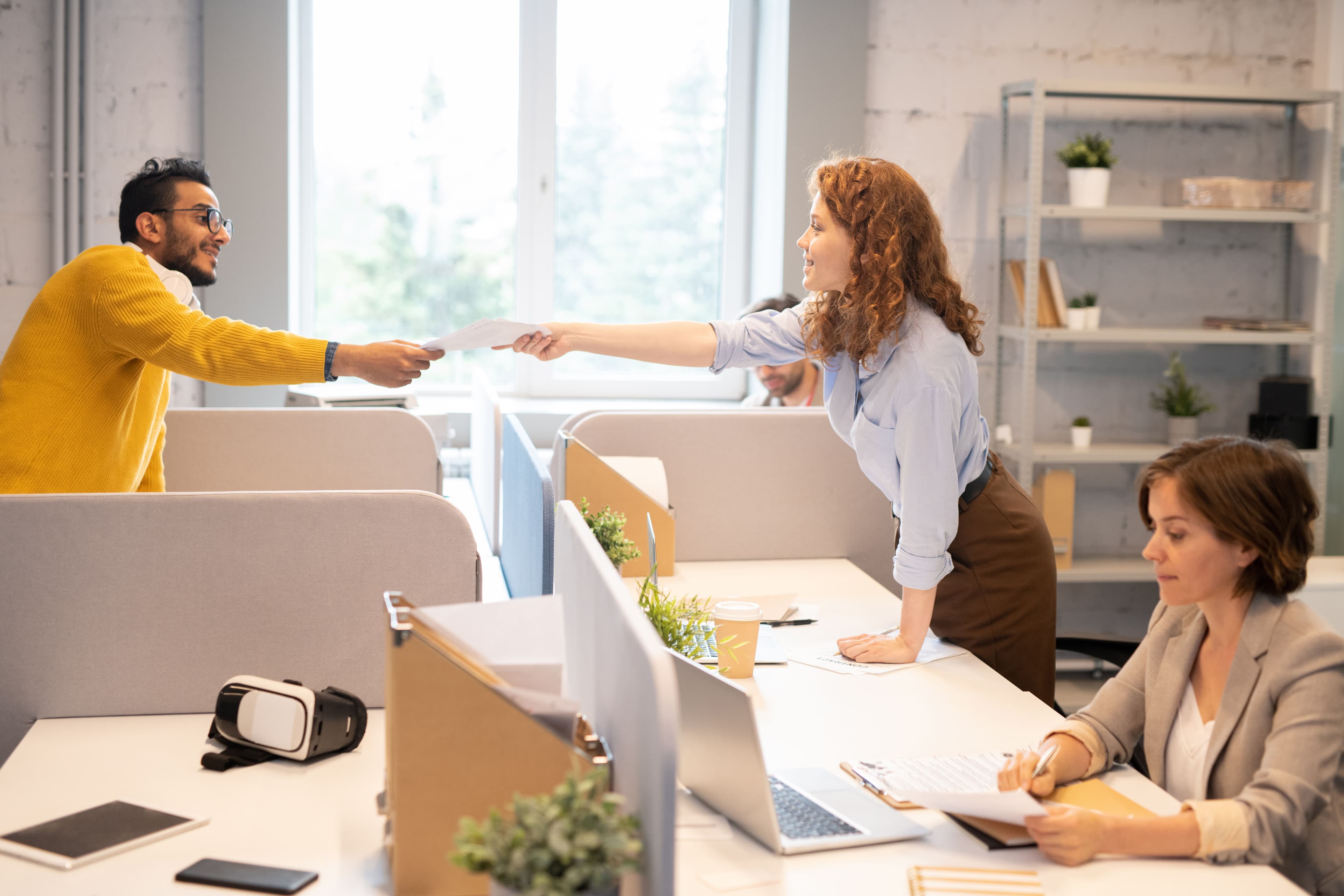  Two colleagues exchanging documents in an open-plan office space, collaborating on a project. This represents "what is digital marketing" by highlighting teamwork and the use of digital tools to optimize marketing strategies.