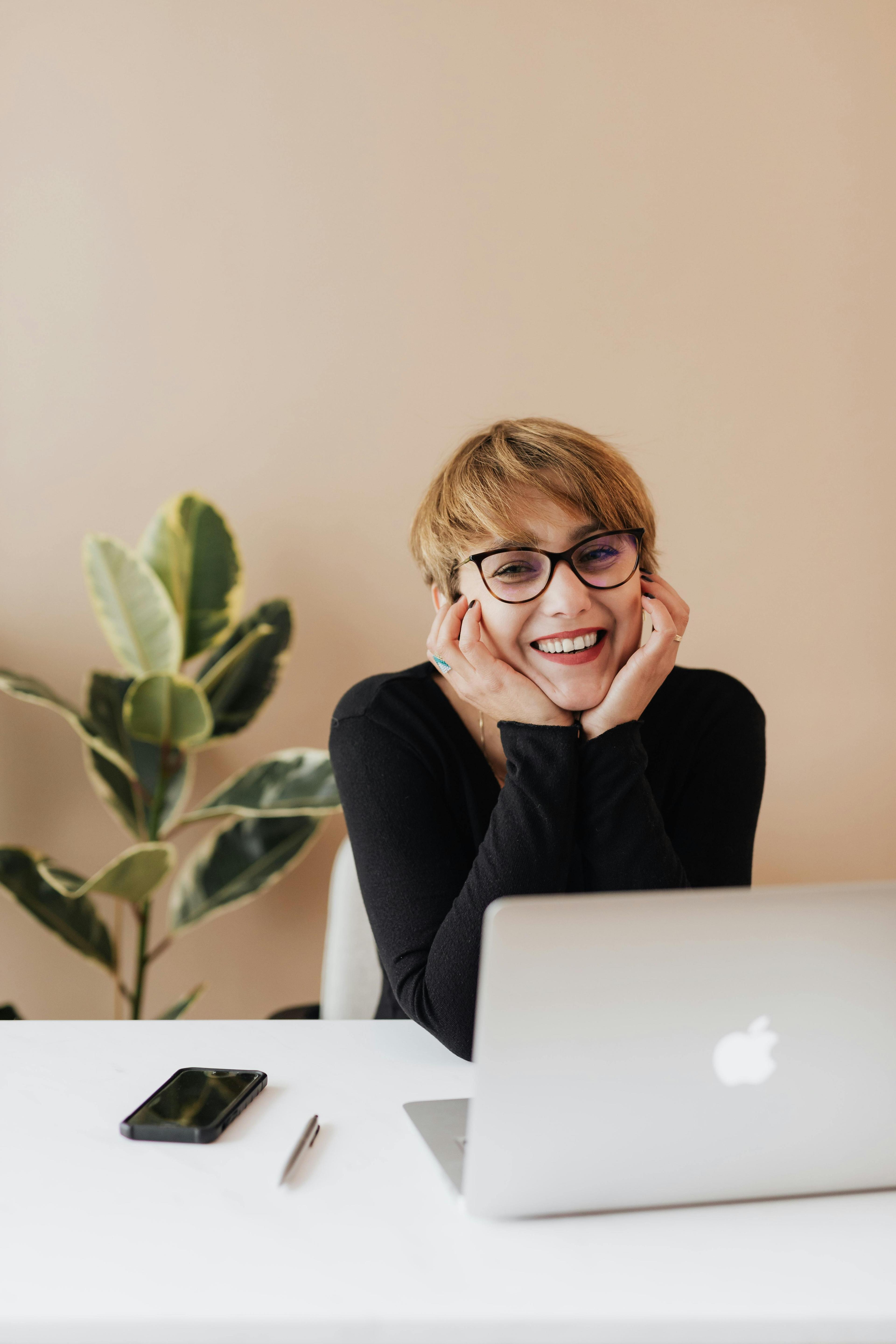 A woman in a cozy indoor setting, smiling as she works on her laptop. The image radiates creativity and independence, ideal for a business that offers custom conversions for mobile workspaces in vans.