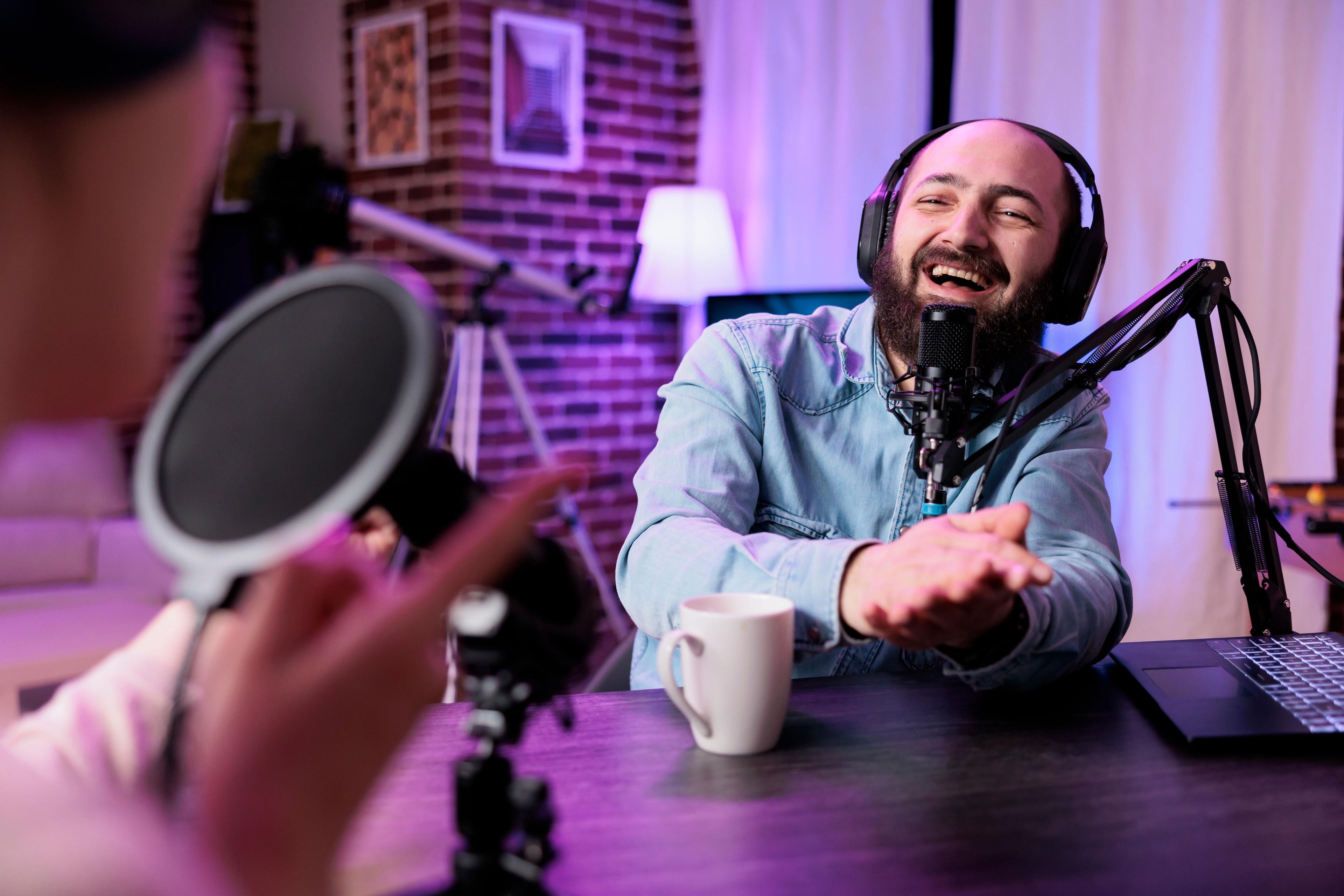 A man with a beard, wearing headphones, laughing while recording a podcast in a studio with vibrant lighting, discussing topics like machine learning techniques such as the train test split in sklearn.