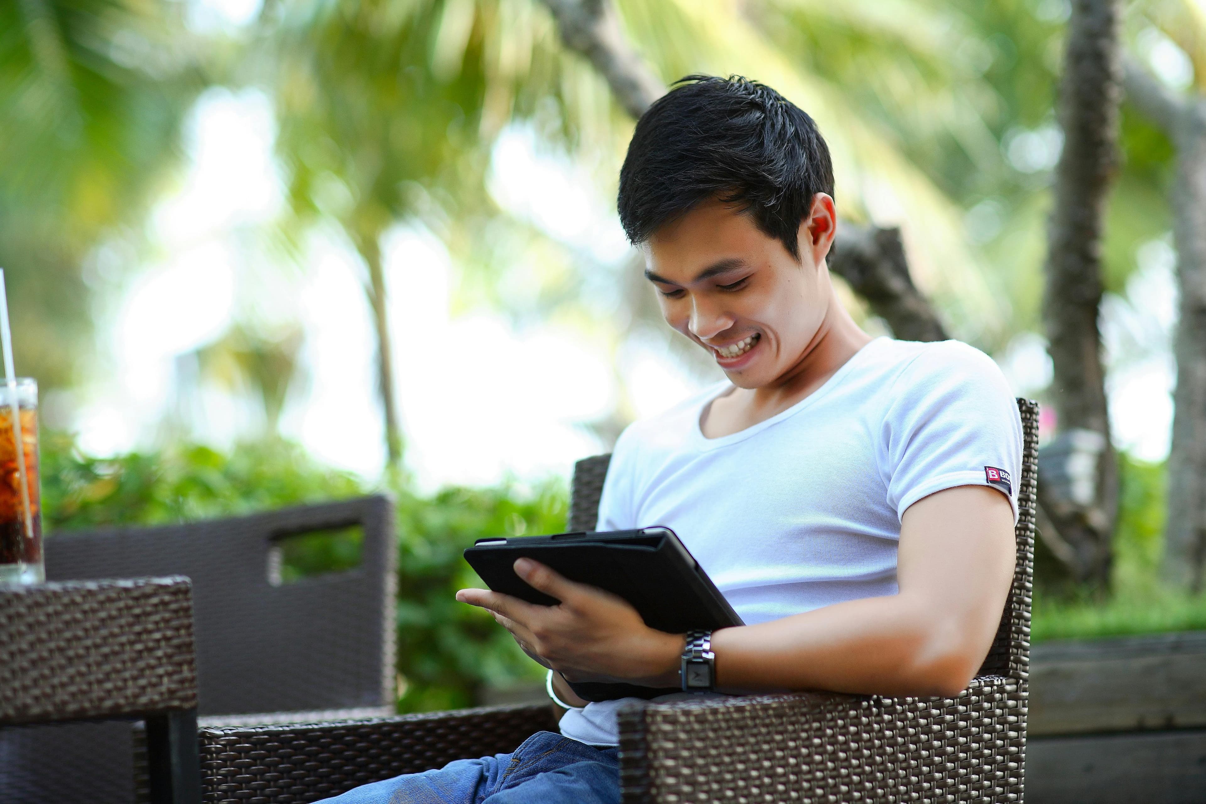 A man sitting outdoors, enjoying a relaxed moment while browsing on a tablet, possibly exploring SEO techniques or digital marketing strategies.