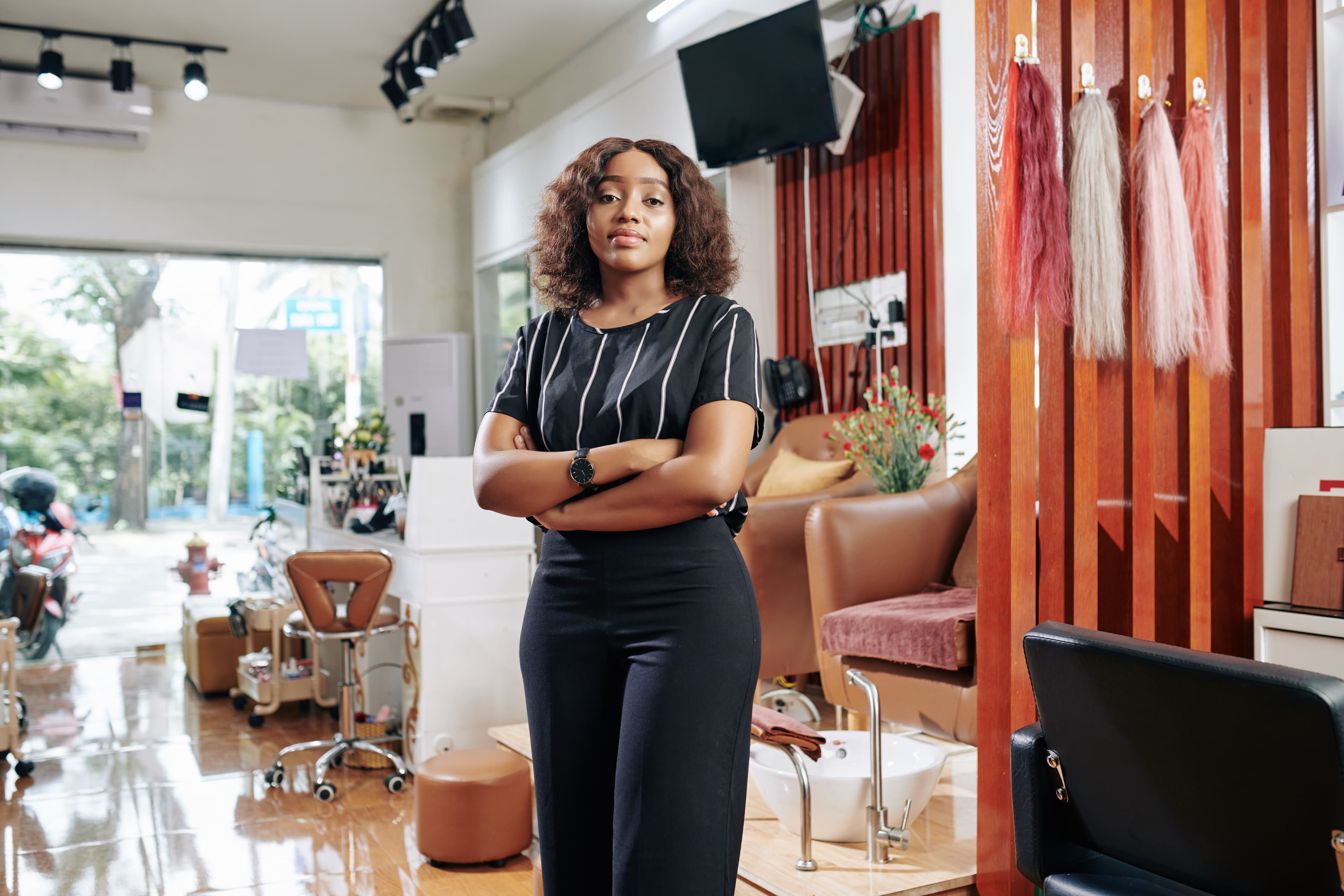 A determined beauty salon owner standing confidently in her business, looking directly at the camera. Her demeanor conveys entrepreneurship and marketing prowess, perfect for a social media marketing job centered around promoting small businesses and local services.