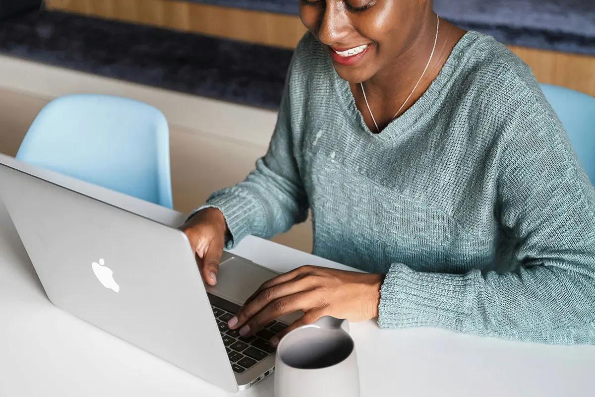 Woman smiling while working on a laptop at a desk, illustrating the work environment related to the competition and markets authority