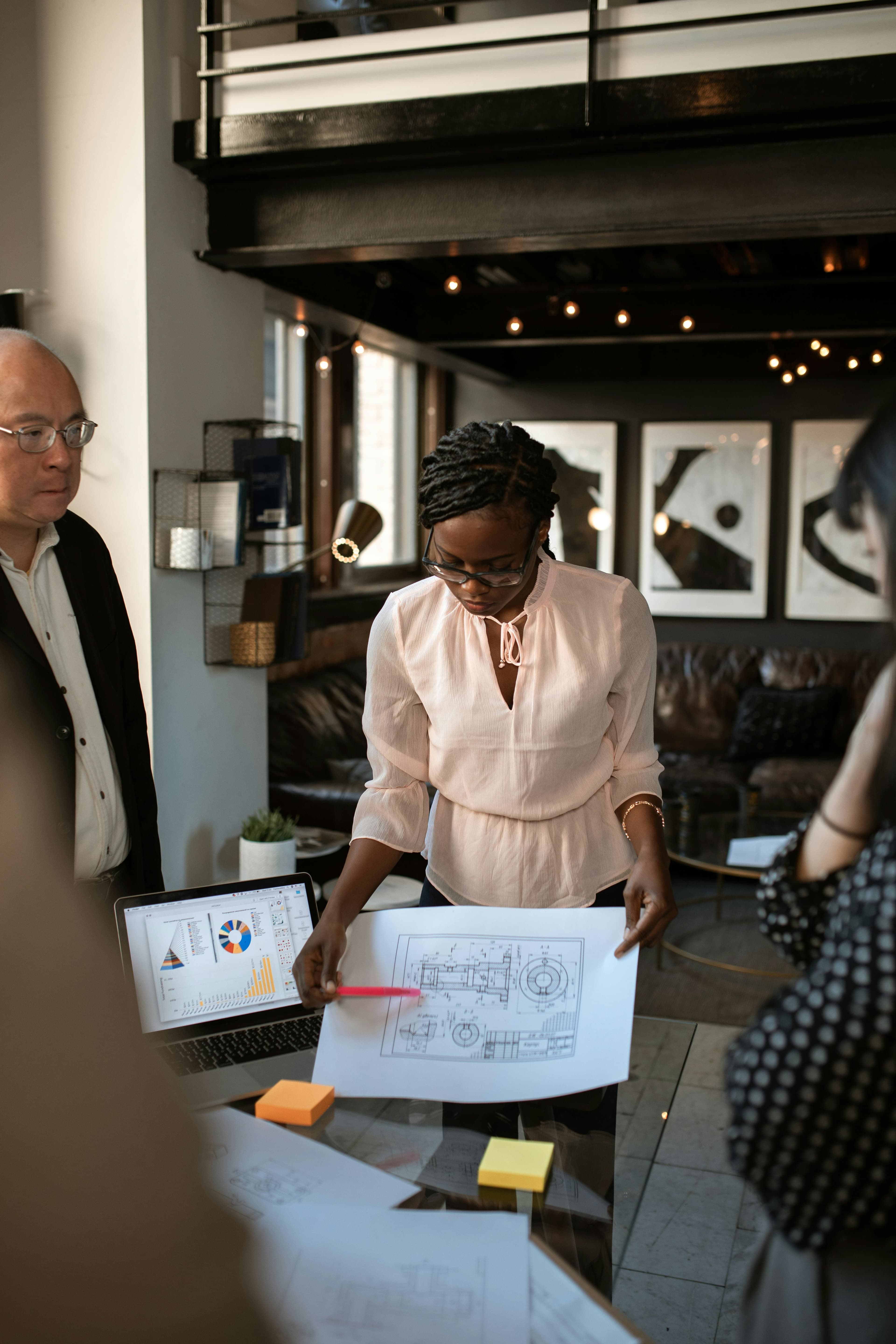 a professional team is gathered in a modern workspace, with one member presenting architectural plans and data charts. This setting could represent a brainstorming session to improve conversion rate optimization, focusing on enhancing user experience and designing better strategies for increasing engagement.