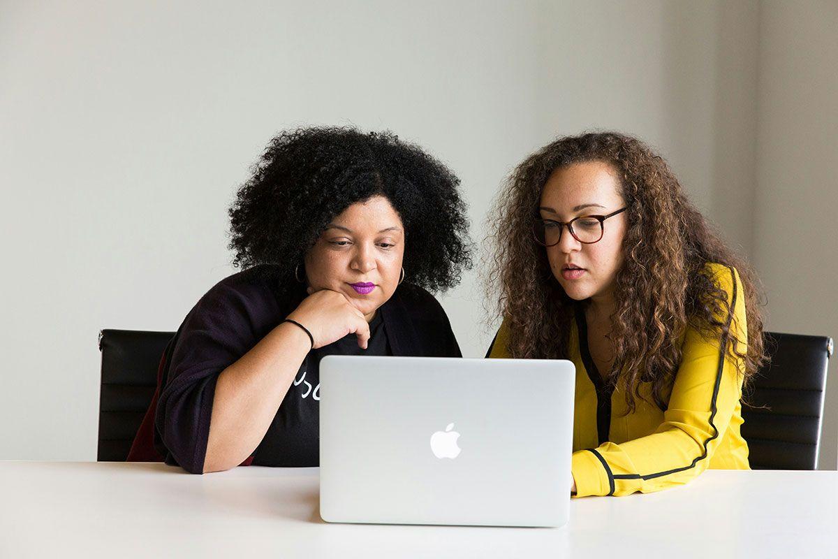 Two women collaborated while looking at a laptop, focused on real estate trends, and suggested research on the real estate housing market crash.