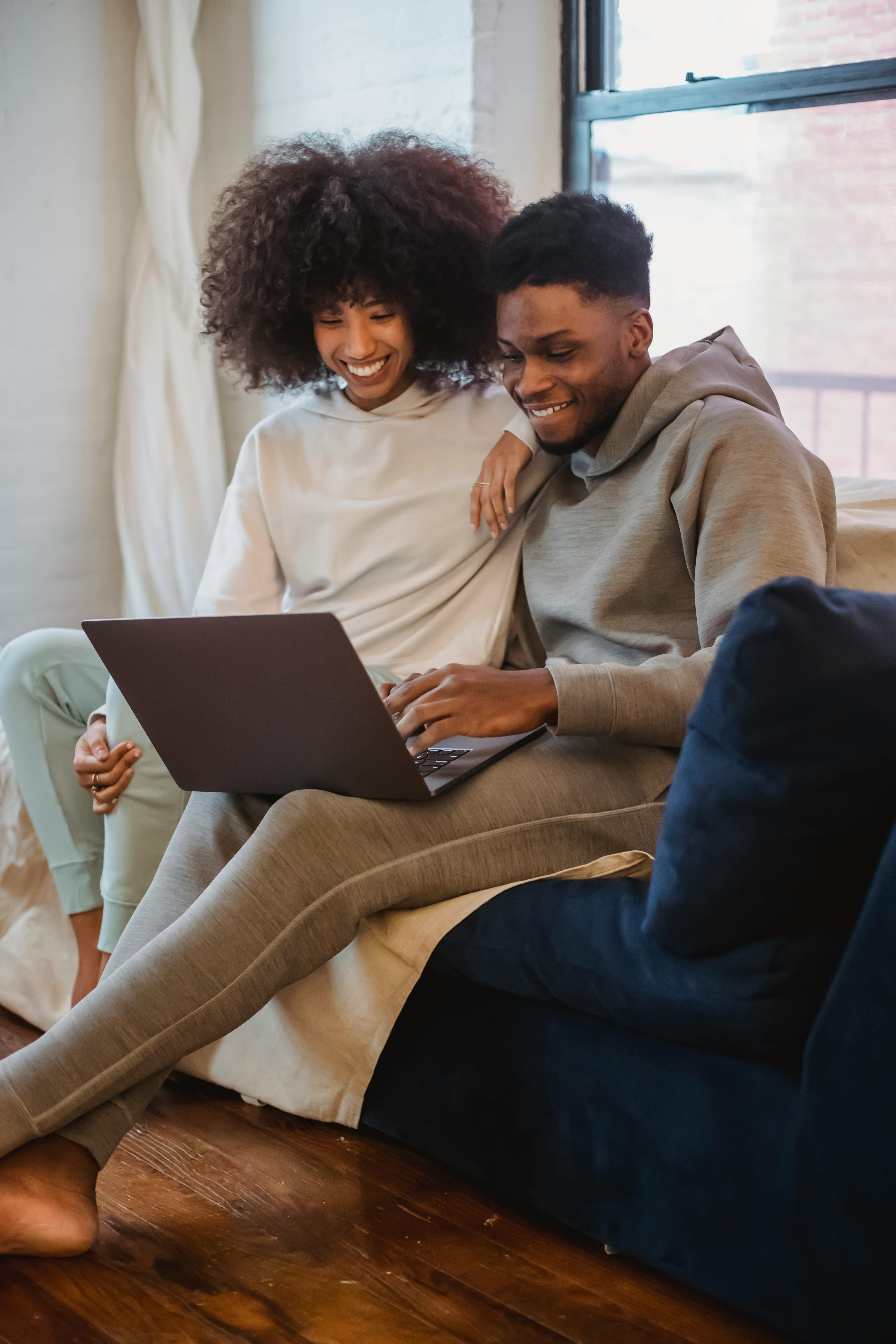 A cheerful couple relaxes on the couch, enjoying time together while using a laptop. This photo fits well with landing page designs emphasizing comfort, connection, or tech-based solutions for everyday life.