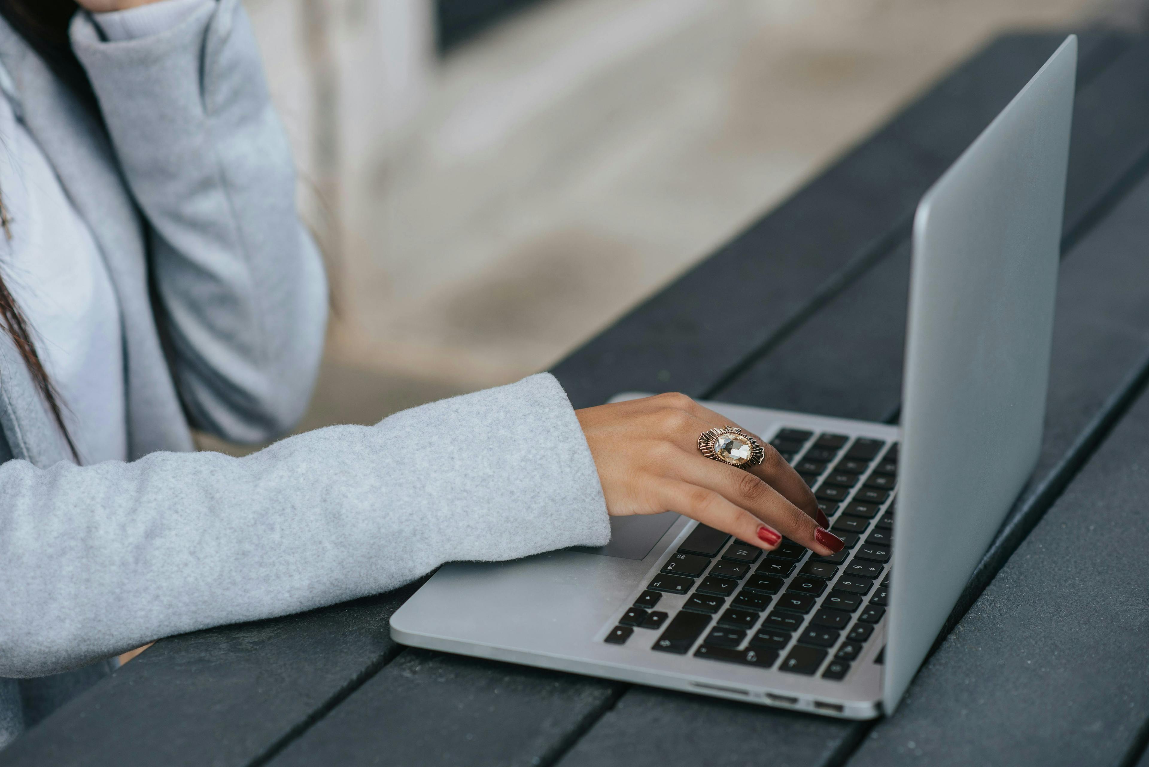 A close-up of a woman's hand typing on a laptop outdoors, focusing on her work. How to market a coaching business.