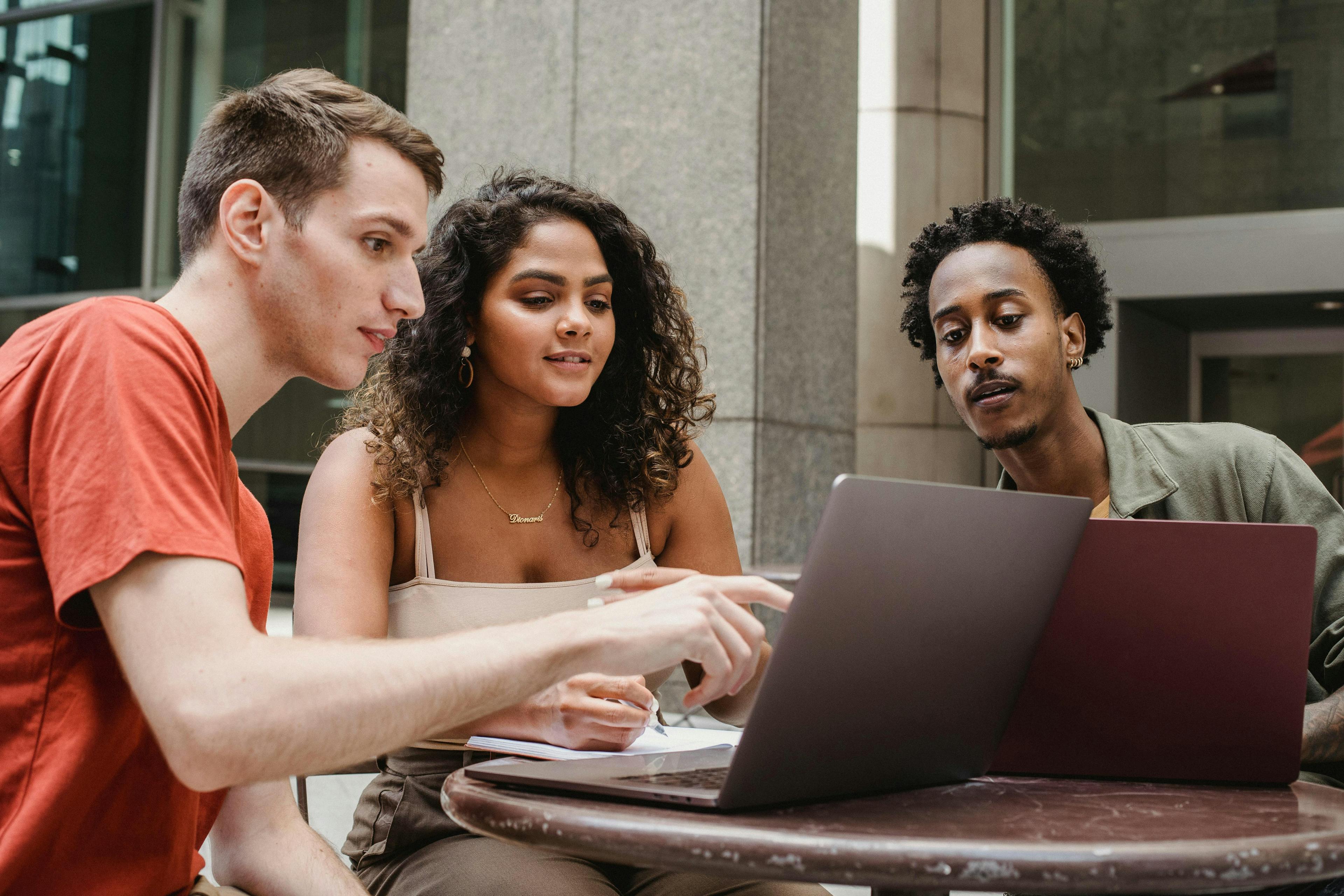 Three people are collaborating at an outdoor table, using laptops and discussing ideas, symbolizing teamwork and modern business strategies. They appear focused and engaged, making it an ideal representation for landing page frameworks.