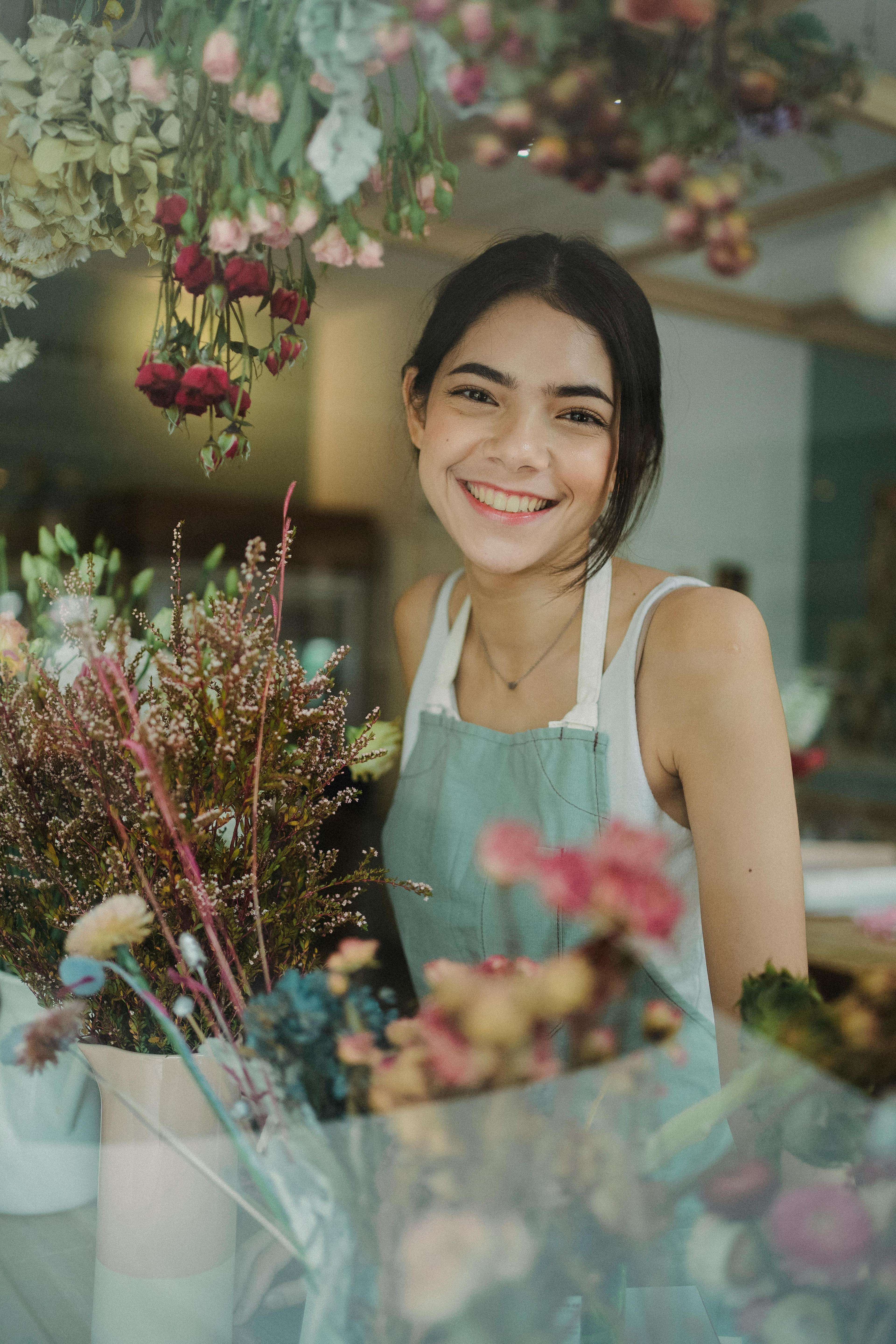  A young florist standing behind a variety of colorful flowers with a cheerful smile, exemplifying creativity and user-focused design skills, essential for UX jobs.