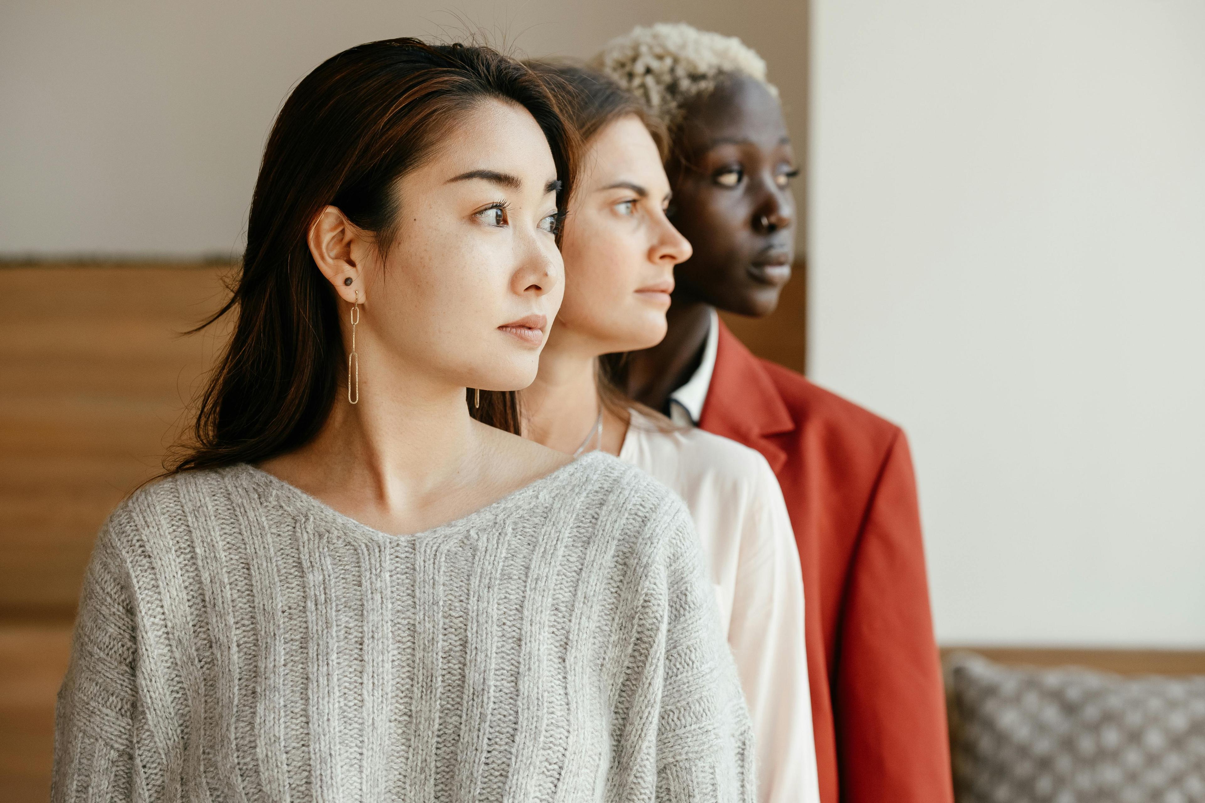  A group of three women from diverse backgrounds standing side by side, looking ahead with a serious expression, highlighting inclusivity and diversity in the context of user experience (UX) jobs.