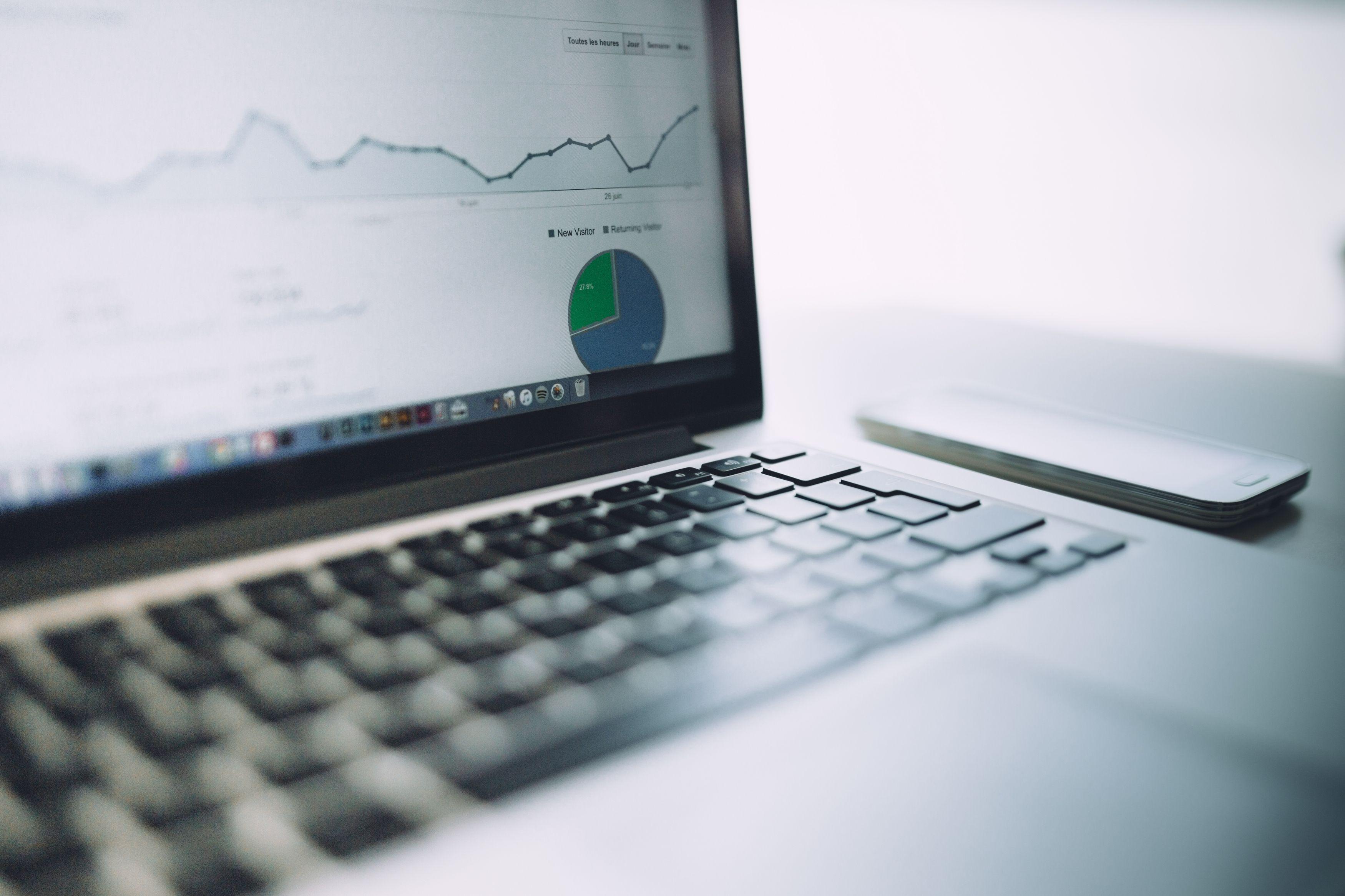 A close-up view of a laptop displaying an analytics dashboard with graphs and a pie chart in a workspace setting, accompanied by a smartphone on the desk. Keywords: train_split_test, data analysis, statistics.