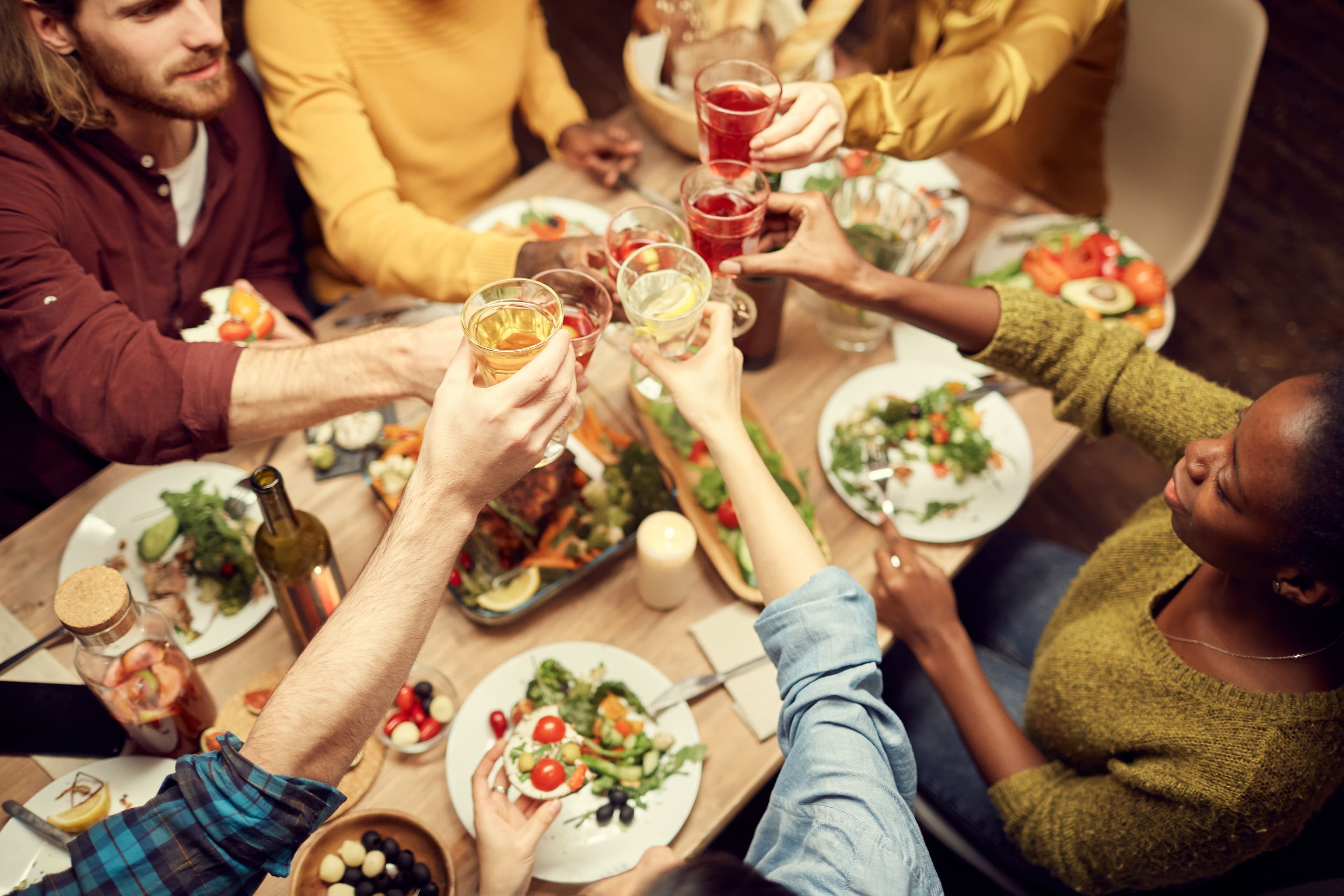 A group of friends gathered around a dinner table, raising their glasses in a toast, celebrating their successful use of tools to track calculator conversion rates for an event they organized.