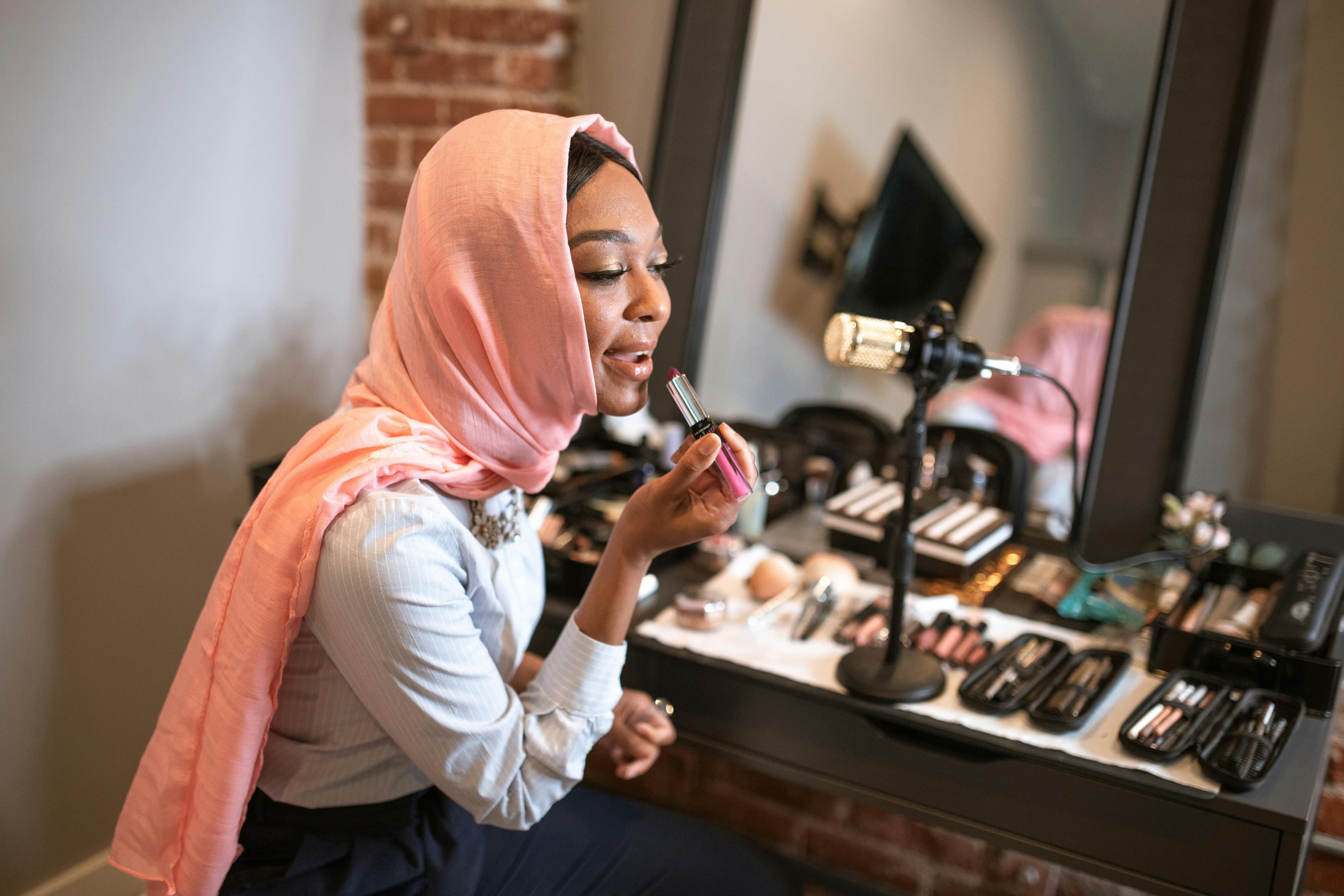 a beauty influencer applying makeup in front of a microphone while recording. This content creation could be part of a video tutorial embedded in top landing pages, designed to attract and convert visitors by offering useful, engaging content.