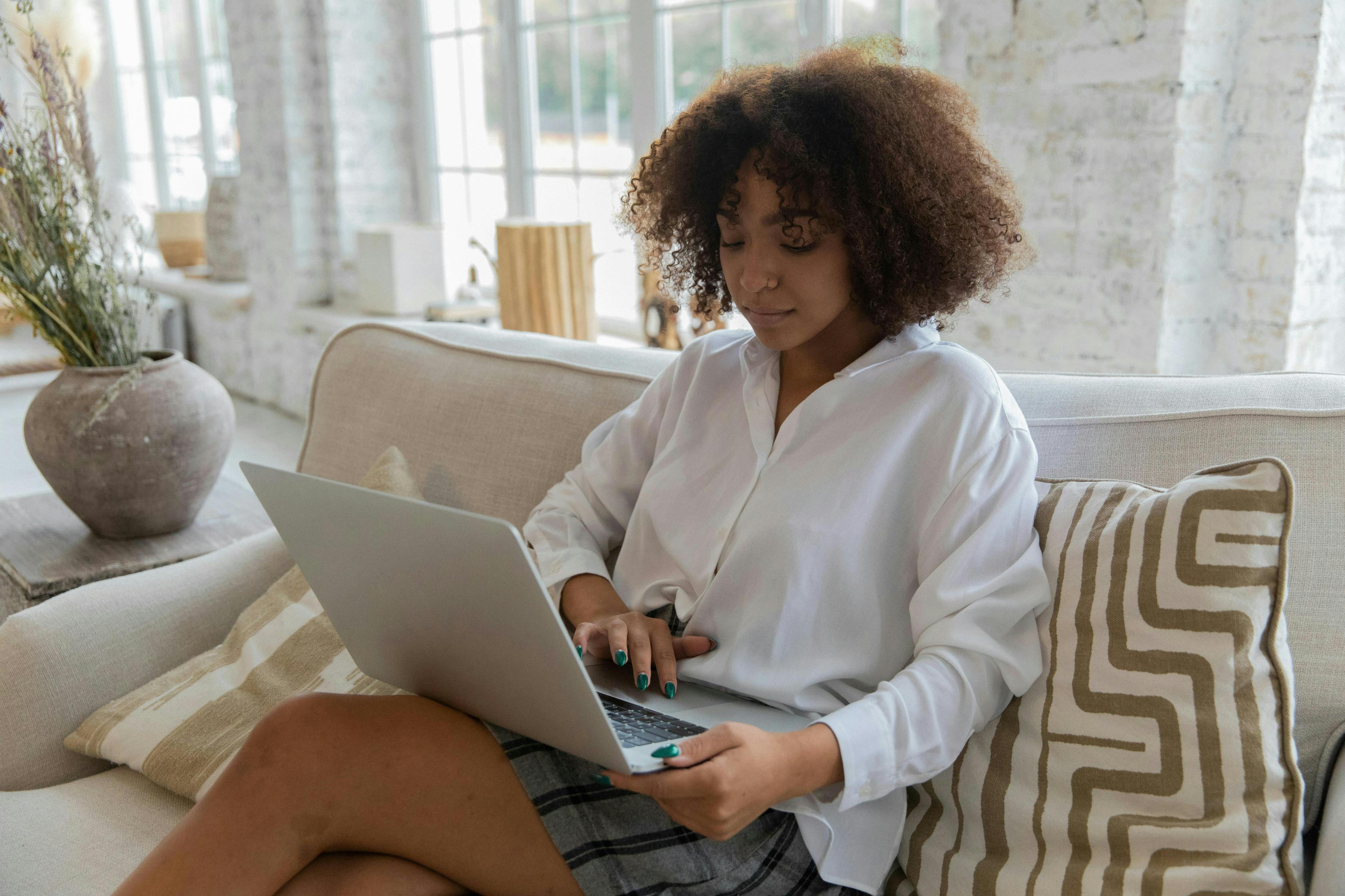  a person sitting on a light-colored sofa, working on a laptop in a bright, airy living space. This comfortable setting is ideal for researching or engaging with "lead generation companies" to boost business opportunities.