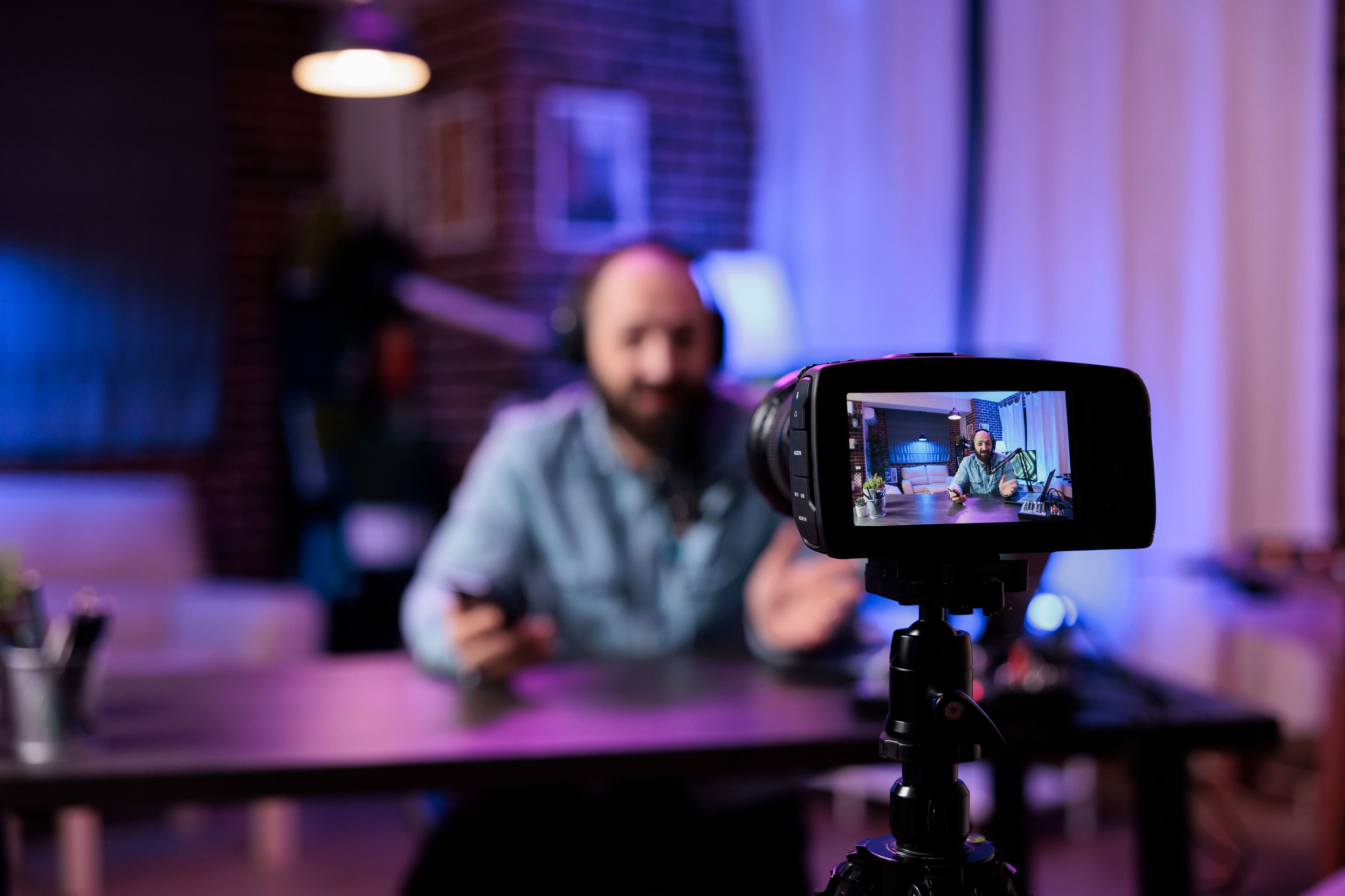 A content creator records a vlog in a studio setting with a camera focused on him. The blurred background and the visible camera screen capture suggest the use of video content as part of a startup marketing strategy to engage audiences online.