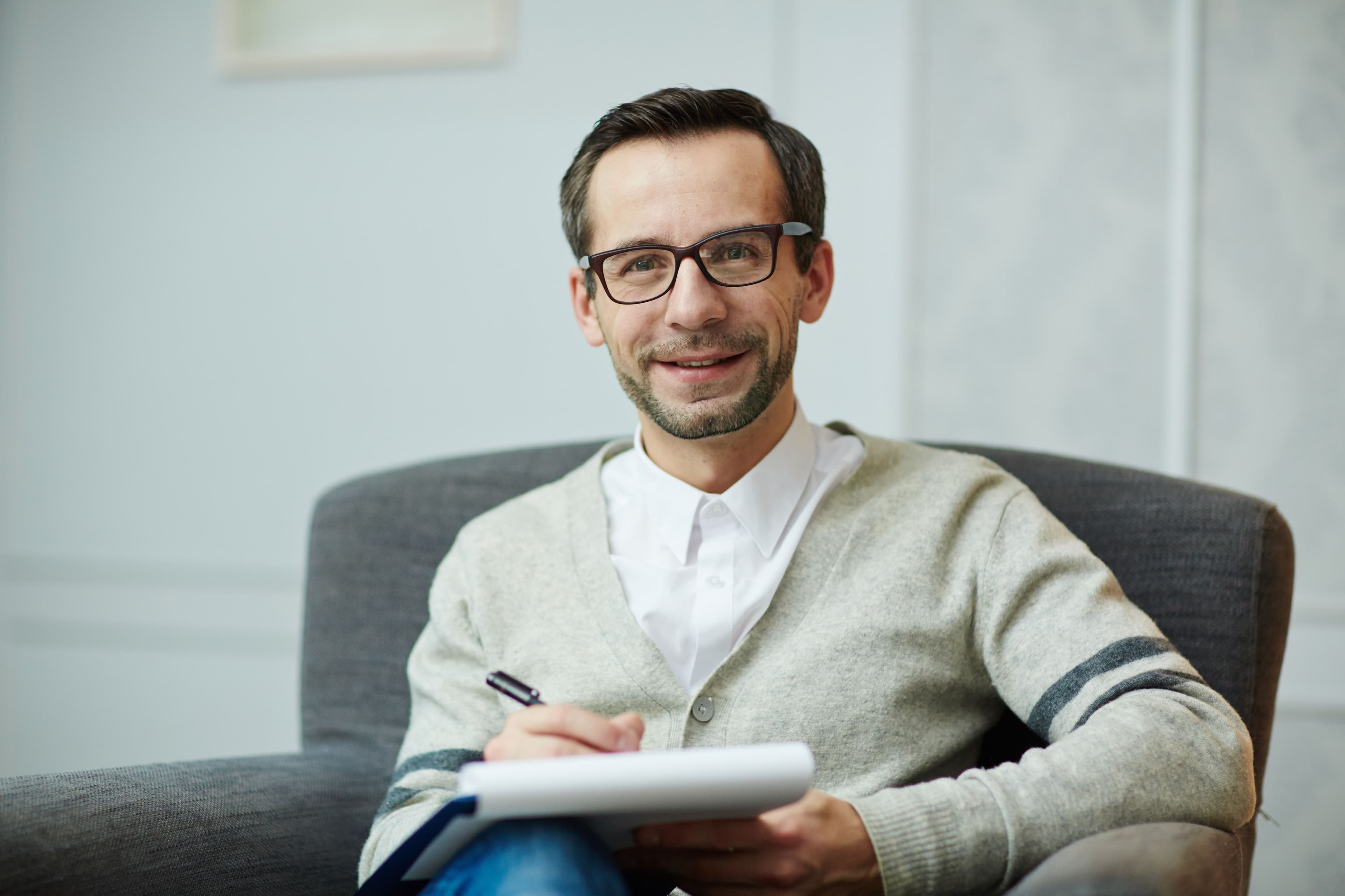 A smiling professional sitting in a modern office, holding a notepad and pen. This captures "what is digital marketing" by depicting a consultant or marketer ready to offer personalized services to help businesses grow their online presence.