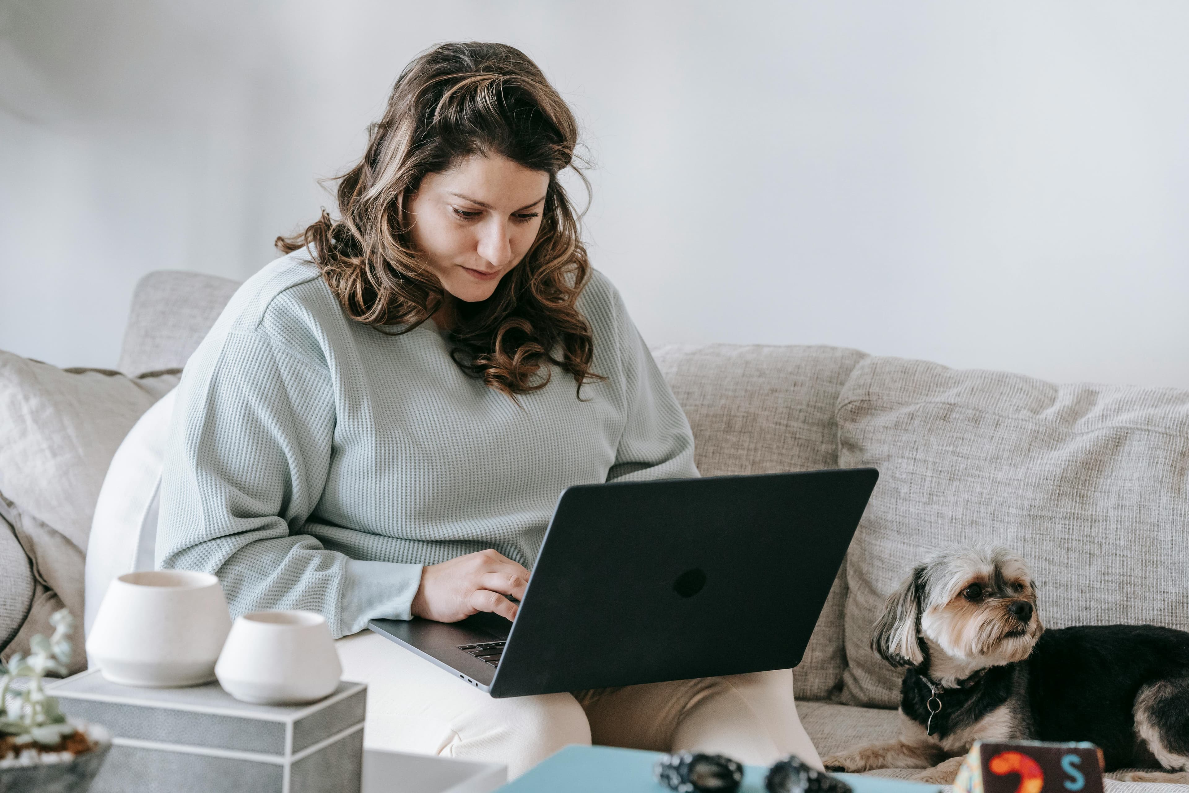 A woman working on a laptop while sitting on a couch at home, with a small dog by her side, representing digital marketing.