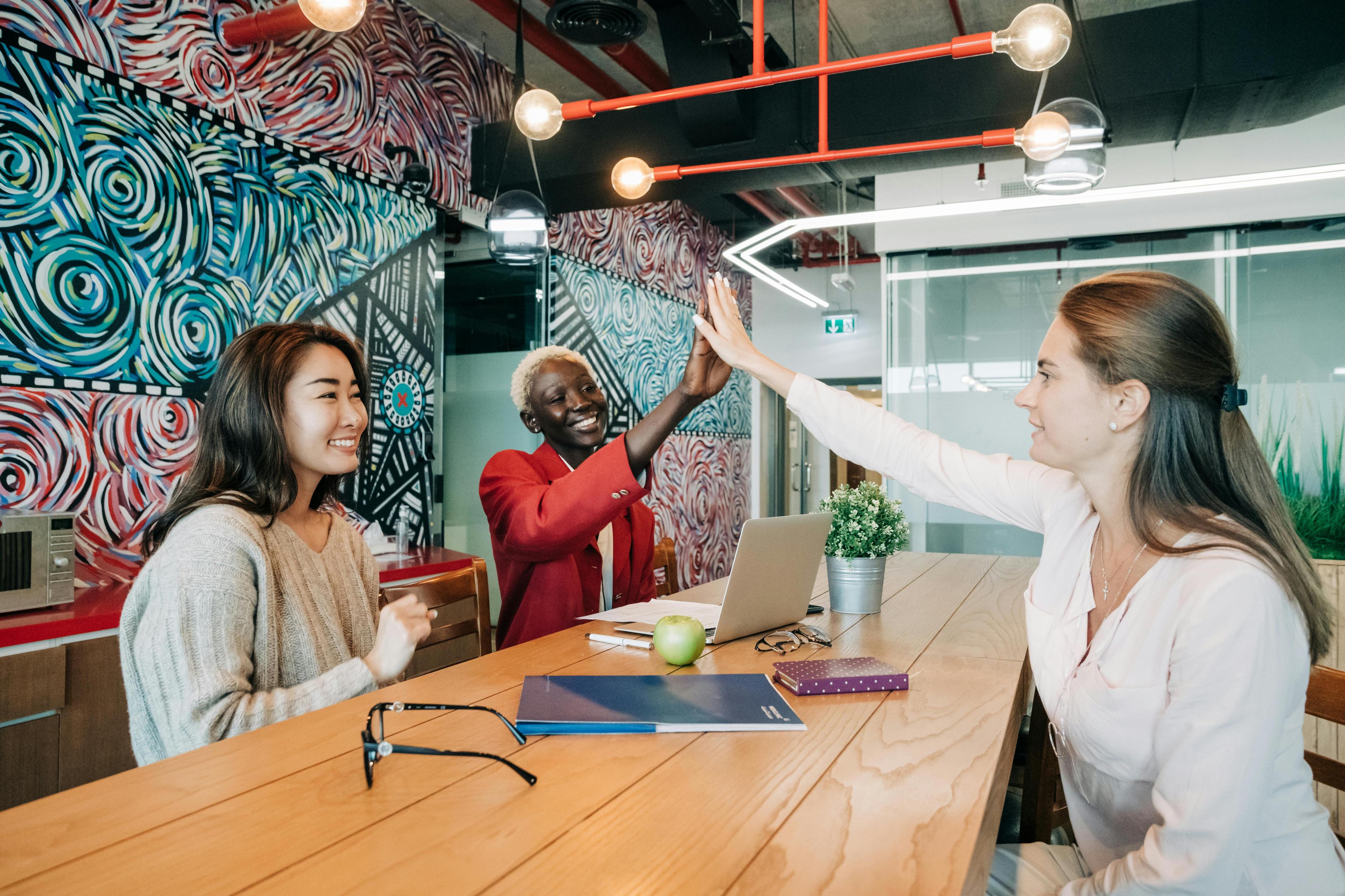 Group of colleagues in a colorful modern office high-fiving and smiling, representing a successful content marketing strategy.