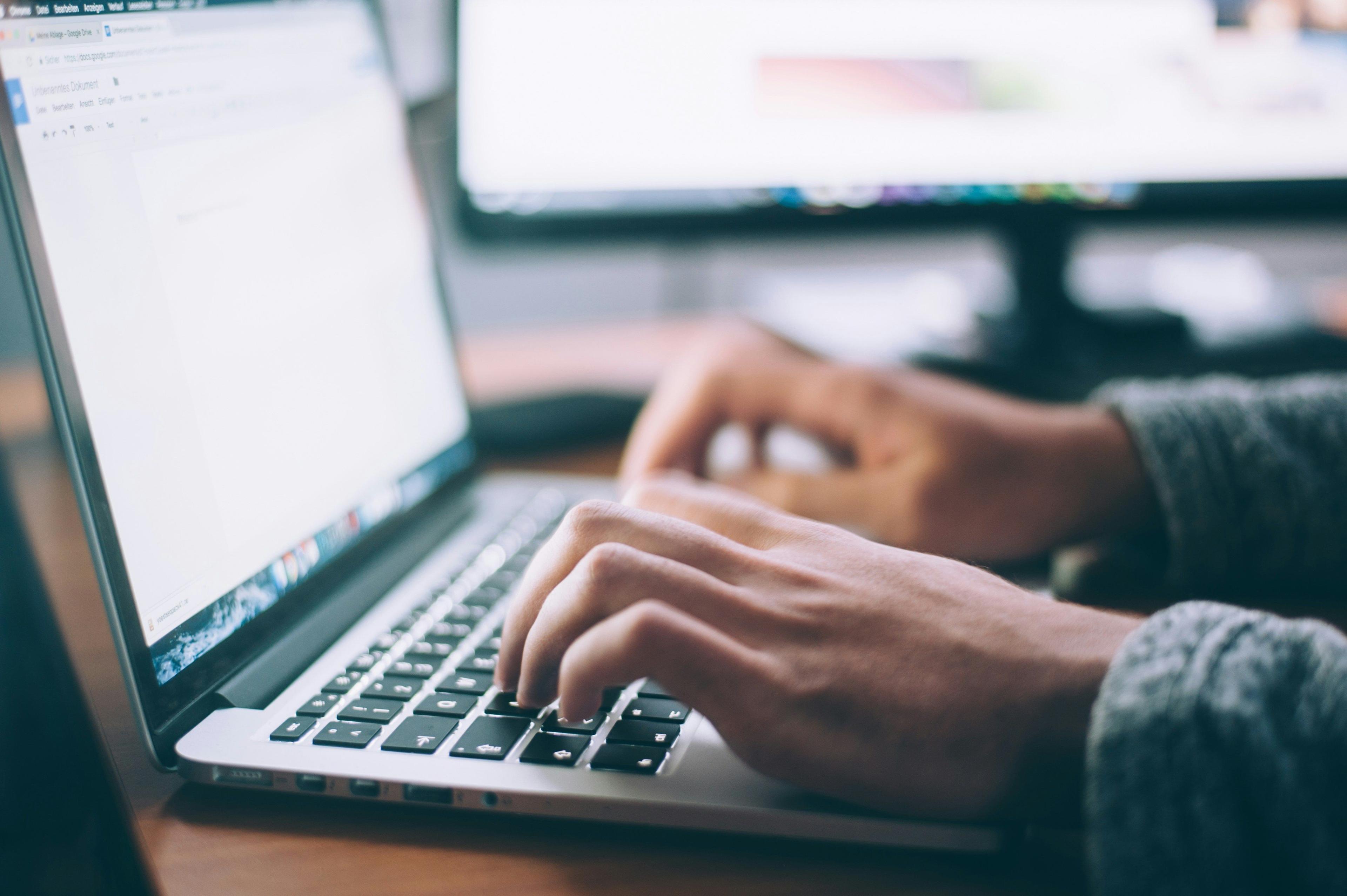 A close-up of hands typing on a laptop keyboard, focusing on a document, perhaps inputting figures into a system to track conversion calculator results for a project.