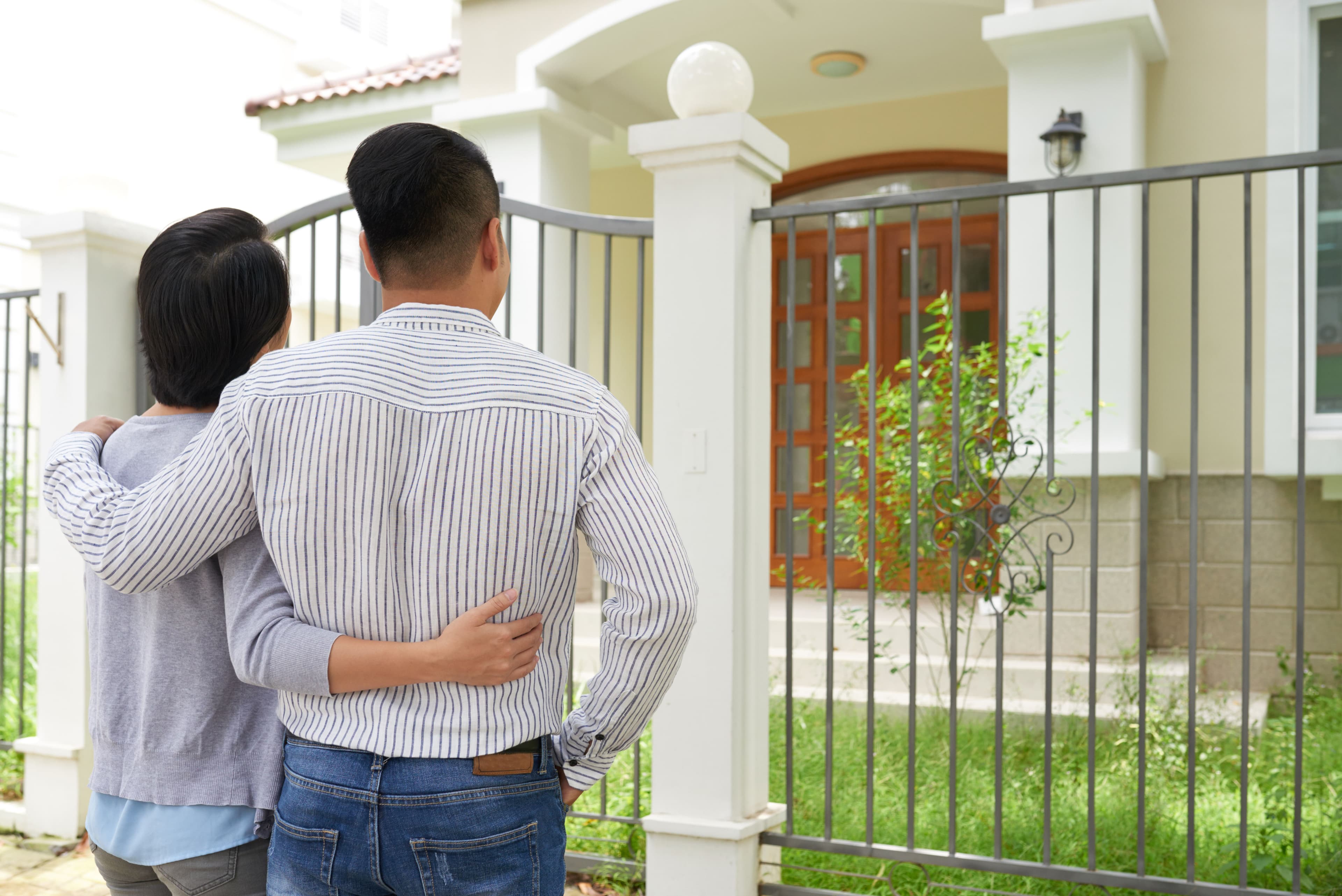 A young couple stands closely together, one person pointing at a modern house, contemplating its purchase. This image suggests split testing for pricing by exploring various real estate options and market pricing.