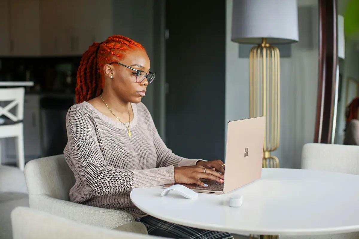 Woman with red hair and glasses working on a laptop at a round table in a home setting, illustrating content marketing.