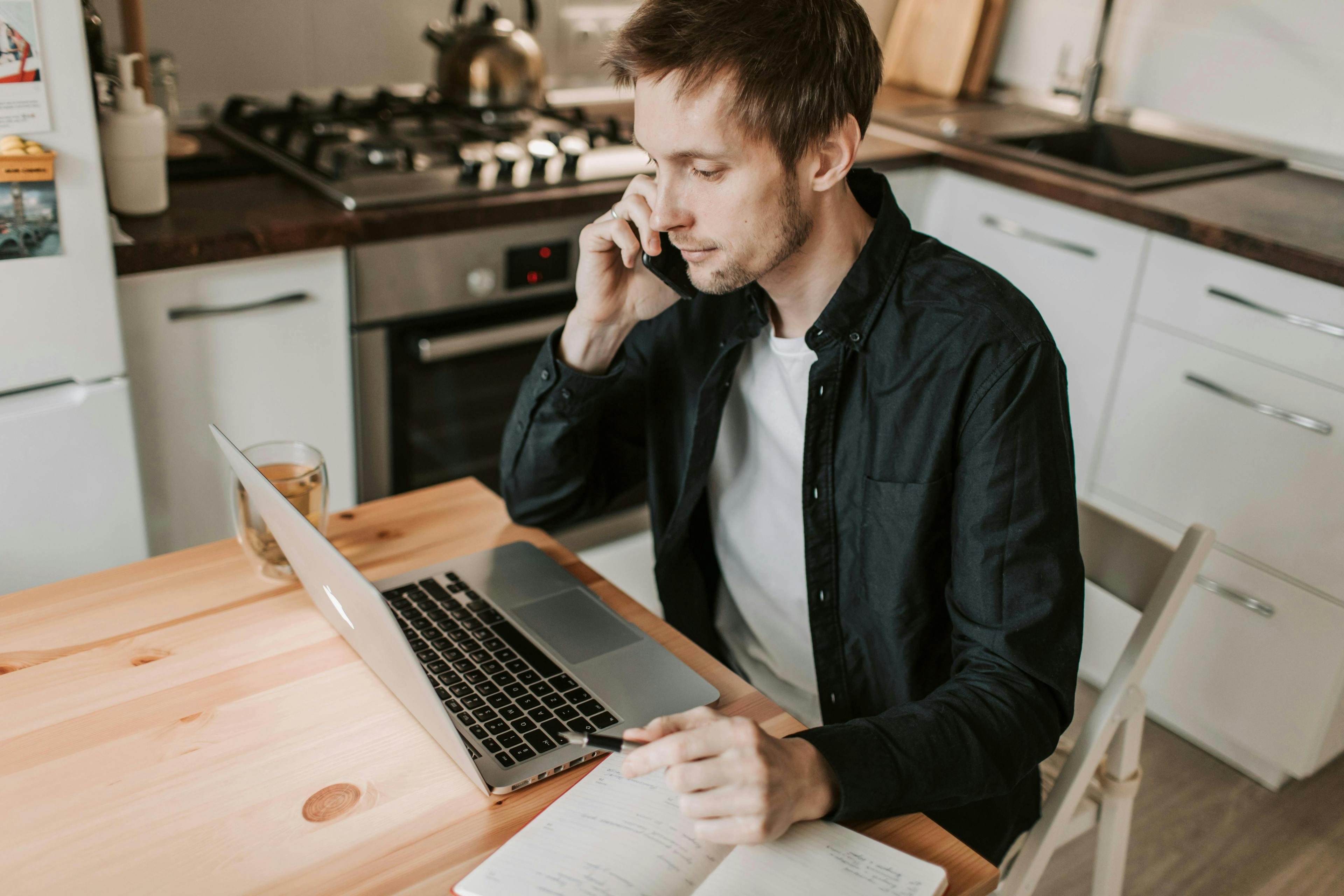 A man working from home, talking on the phone while taking notes, representing the flexibility and personalized approach offered by a marketing agency for startups.