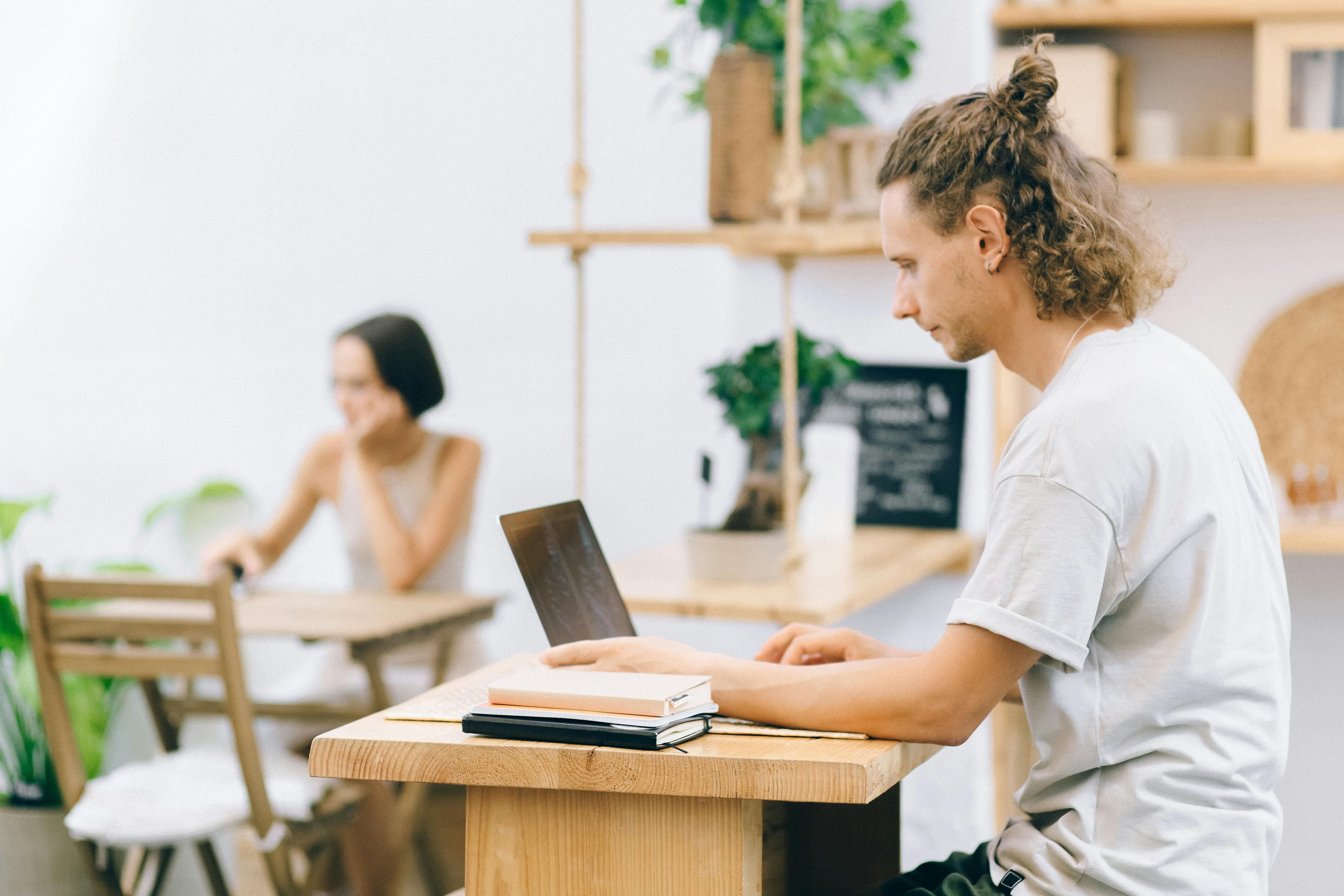 A young man with curly hair and a man bun working on a laptop in a cozy café setting, representing digital marketing for financial services.