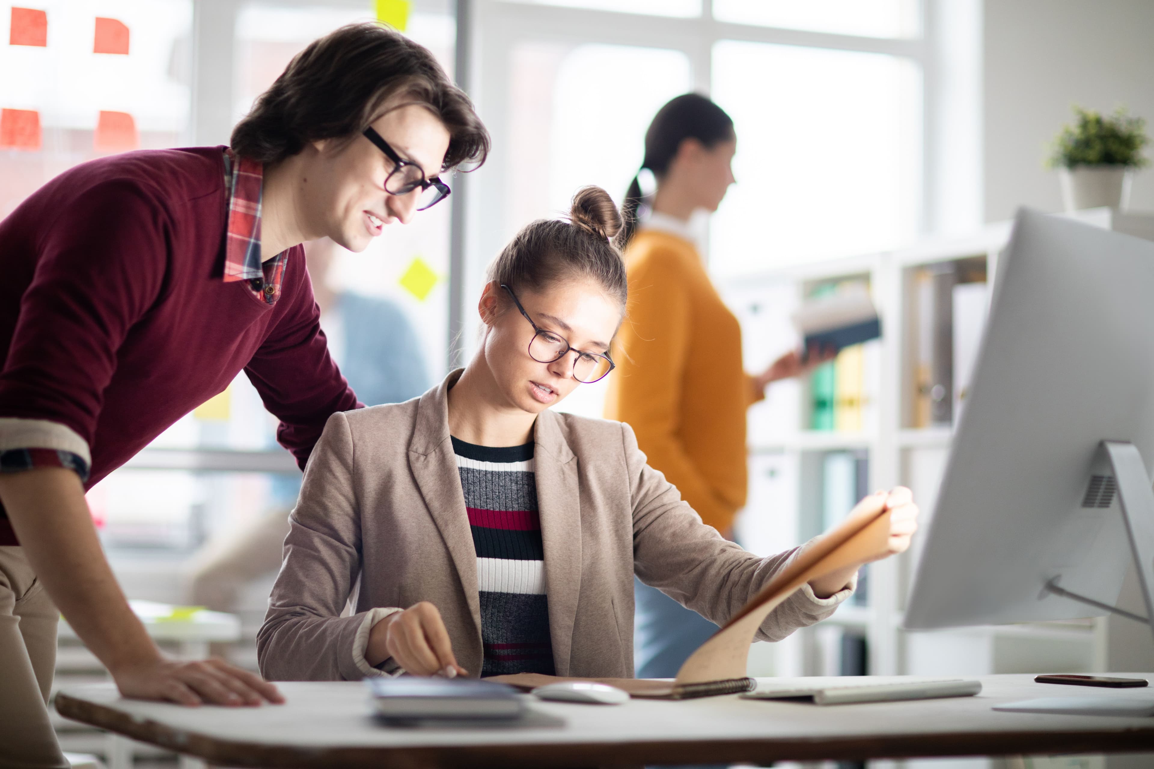 Two colleagues discussing a document while working together in a bright, collaborative office. This visual reflects "what is DTC marketing" by highlighting teamwork within direct-to-consumer companies as they develop targeted marketing plans to engage their customer base.