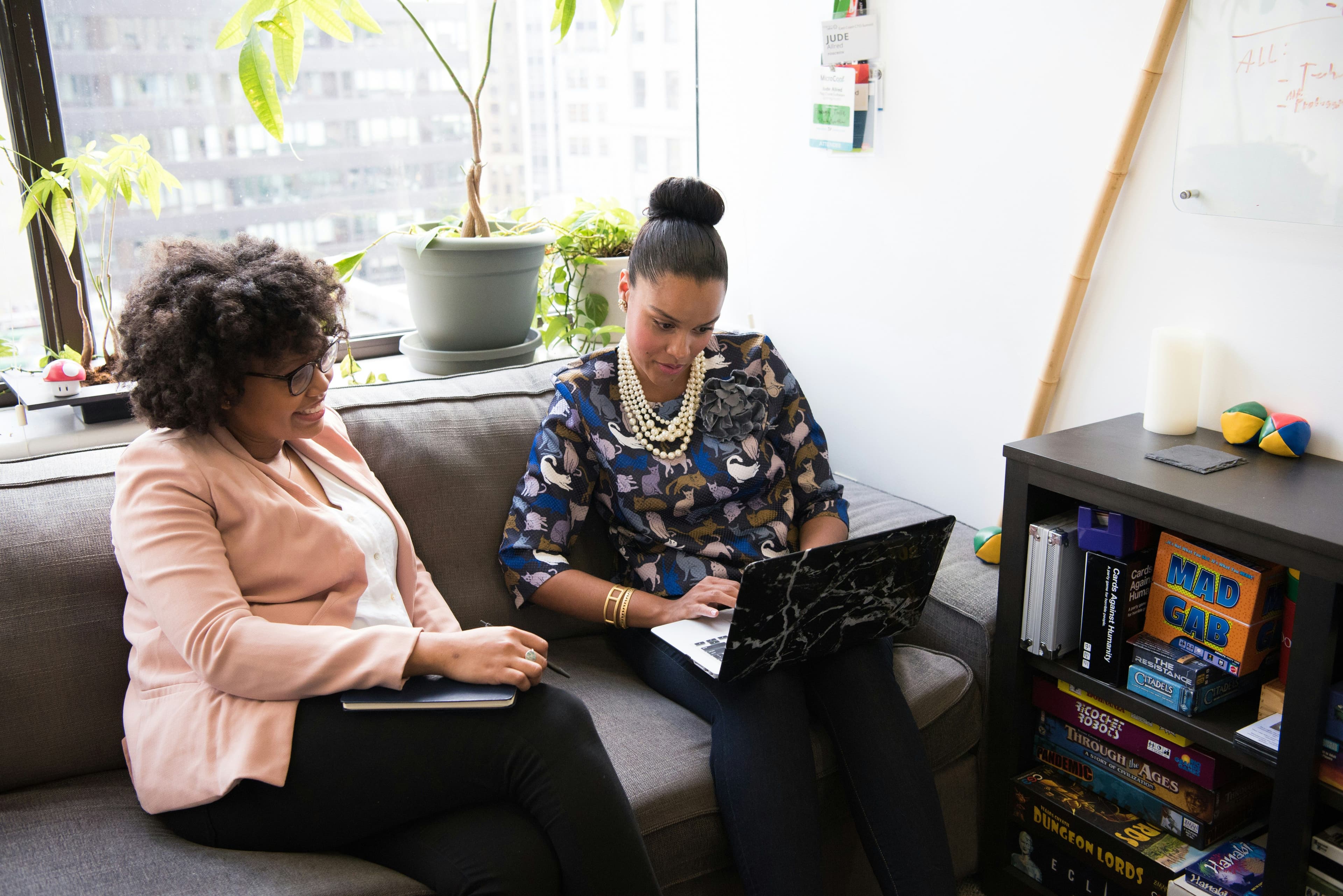 Two women collaborating on a laptop in a modern office environment, exemplifying teamwork and strategy planning for social media marketing campaigns.