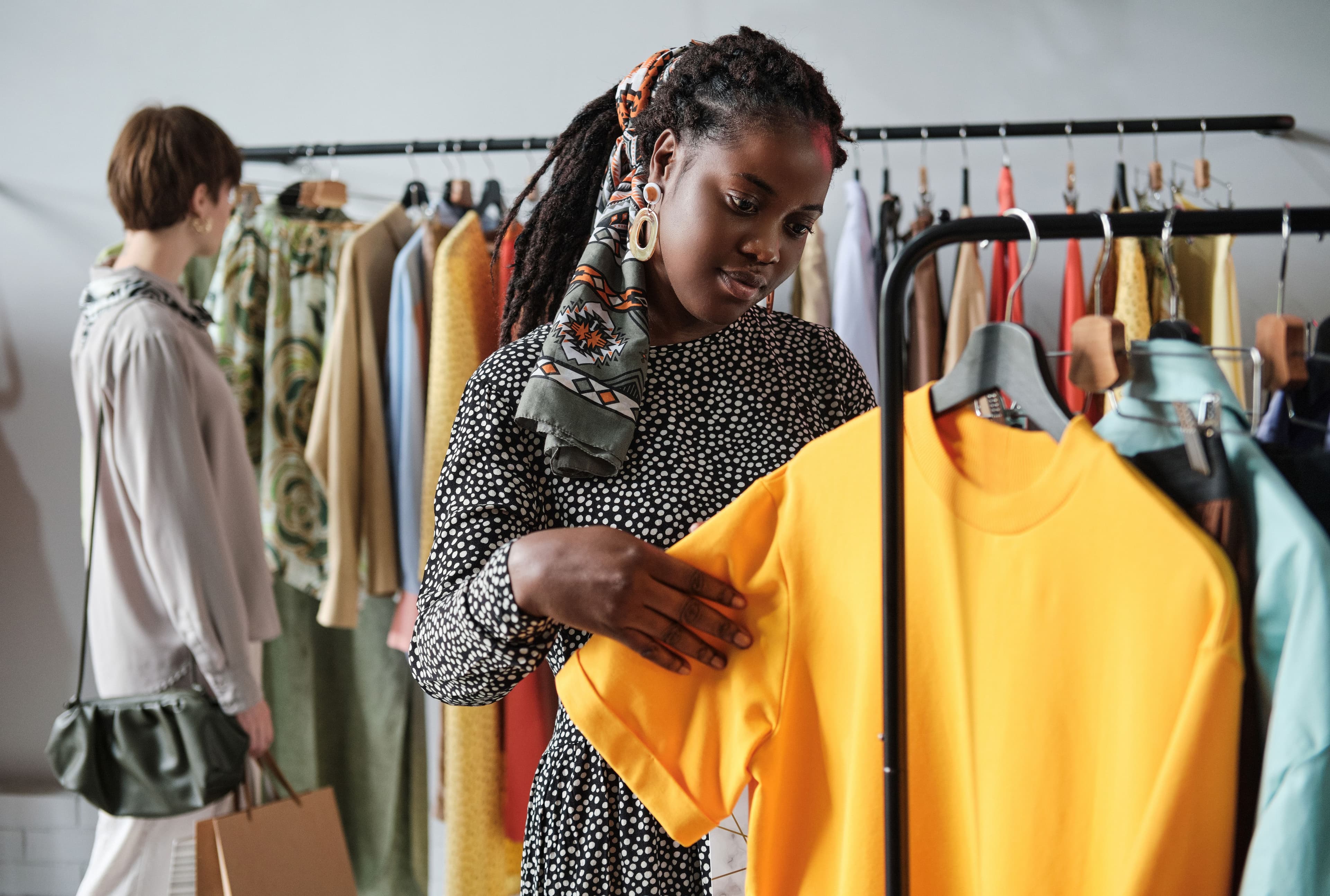 A woman browsing clothing in a boutique, holding a yellow top and inspecting its quality. This image illustrates "what is digital marketing" by showing how online fashion brands use digital platforms to promote their products and drive in-store traffic.