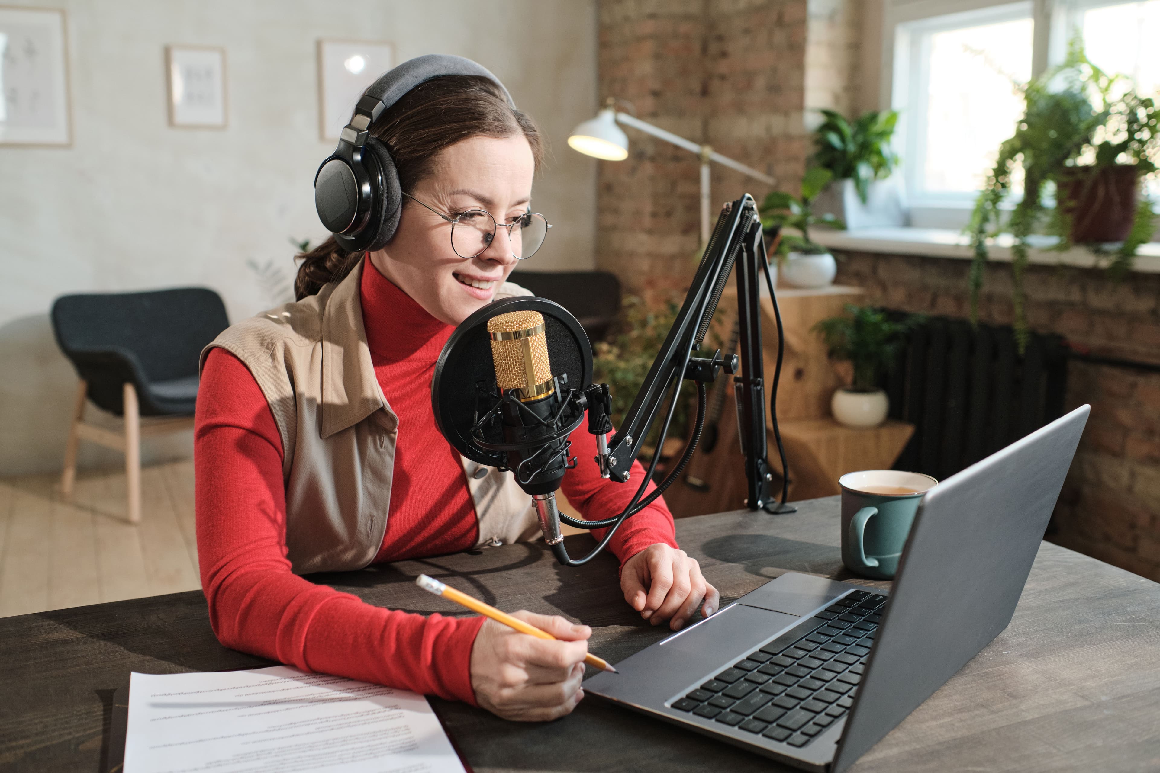 A woman, microphone in front of her, is writing notes while speaking into a microphone, creating content for a podcast or live radio. This scenario could be useful for testing different scripting techniques through A/B testing to improve audience retention. Keywords: a b testing definition, podcast planning, content strategy.