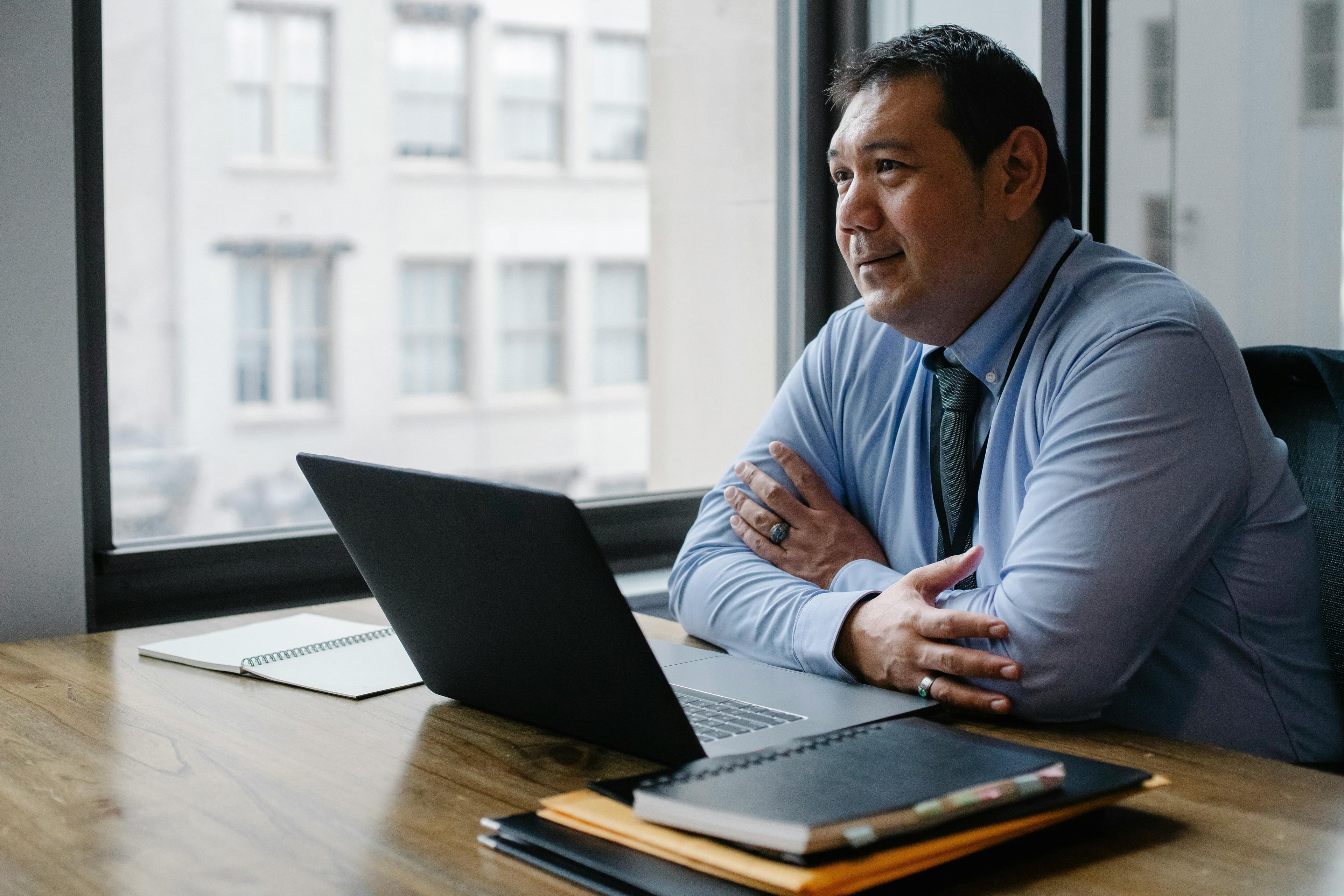 A professional man sits at a desk with a laptop, looking thoughtfully out of the window, symbolizing a strategic approach to understanding 'what is SEO marketing?' in the digital business world.