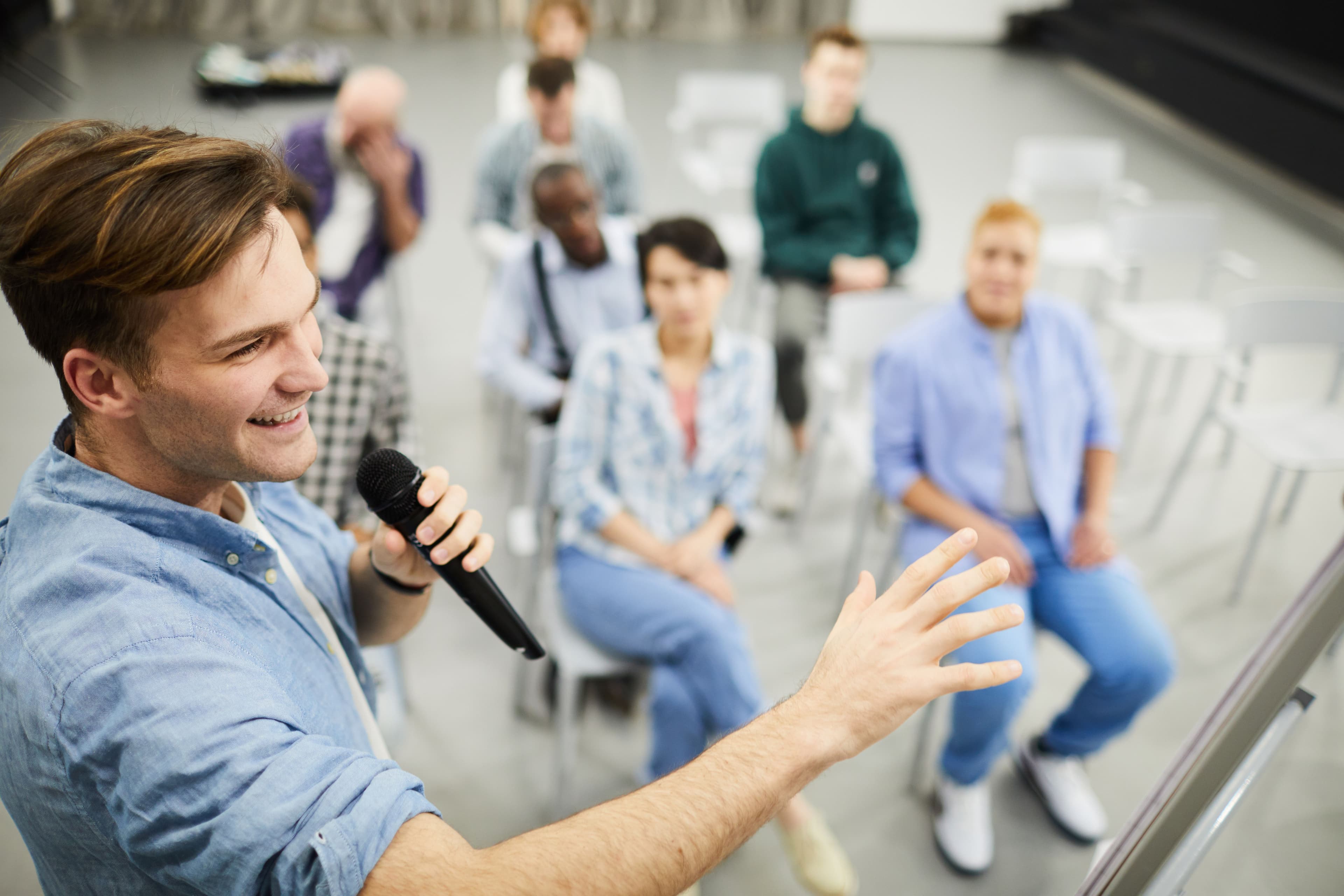 A small business marketing consultant speaking to a diverse audience, holding a microphone, engaging in a workshop or seminar on effective marketing techniques.