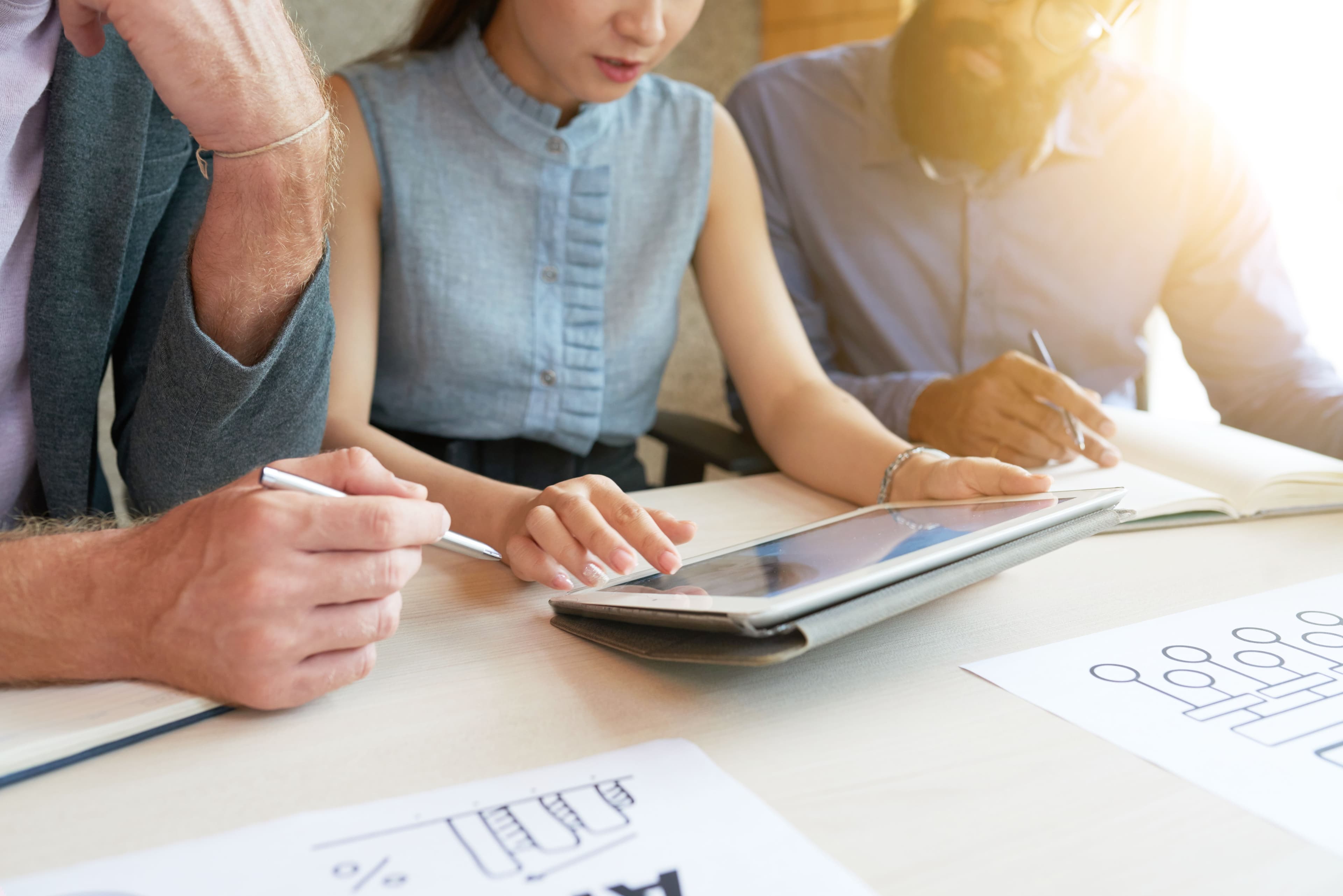 Close-up of three colleagues collaborating at a desk, focused on a digital tablet, brainstorming social media marketing strategies. This image represents social media marketing jobs that involve teamwork and innovative digital campaigns.