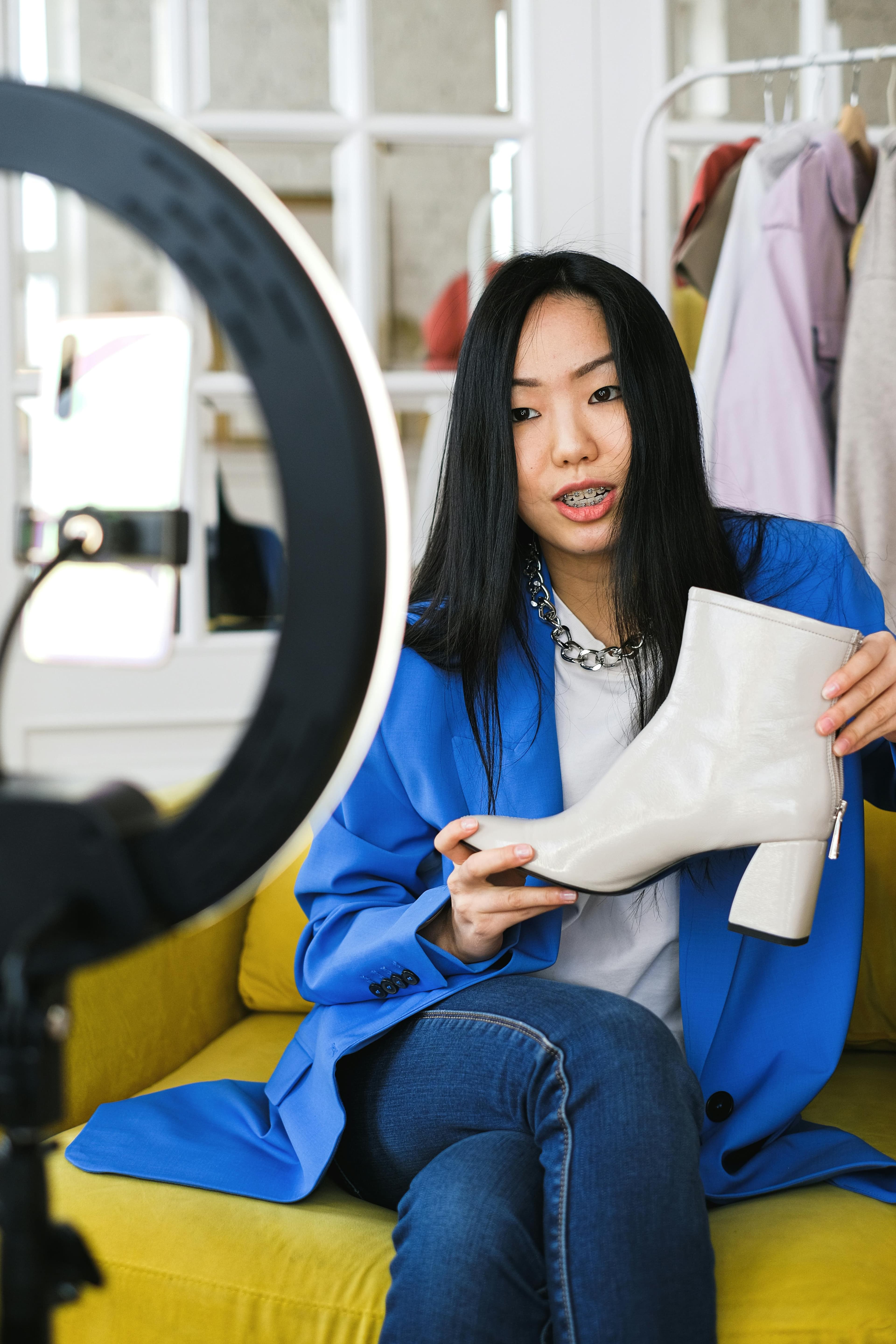 A fashion influencer sitting on a couch, showcasing stylish white boots to a camera with a ring light, representing how clear, professional presentations on websites that convert can drive product sales and brand loyalty.