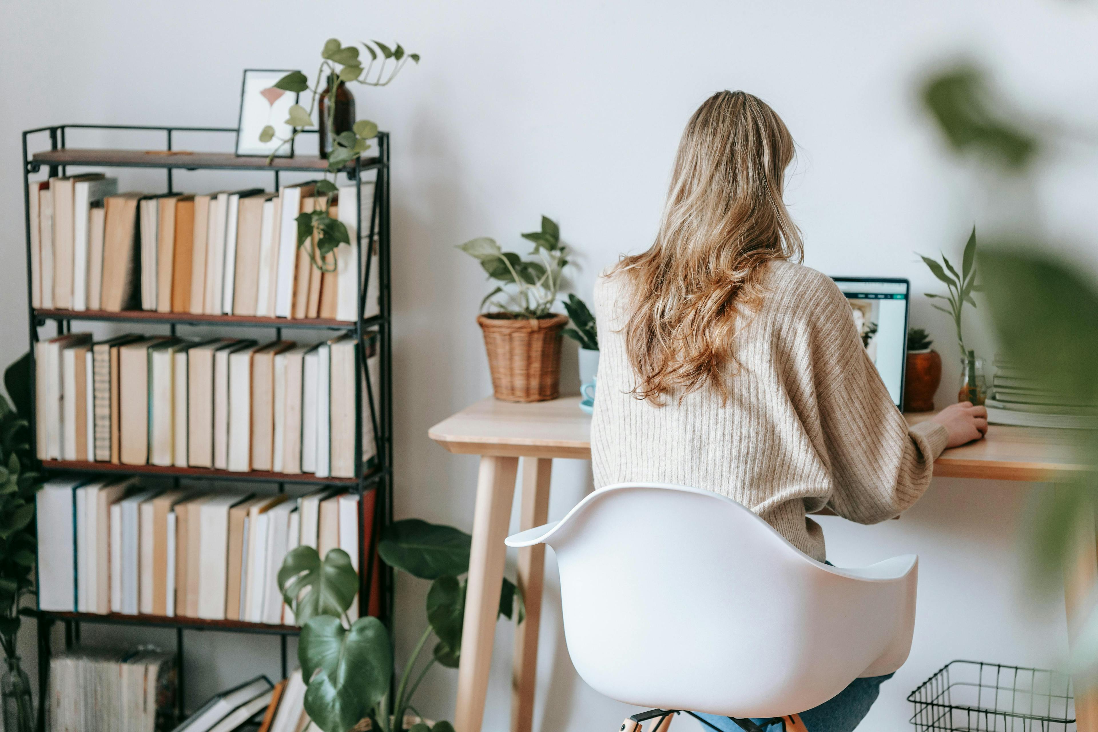 A woman working on a laptop at a desk in a cozy home office with a bookshelf and plants, representing digital marketing jobs.