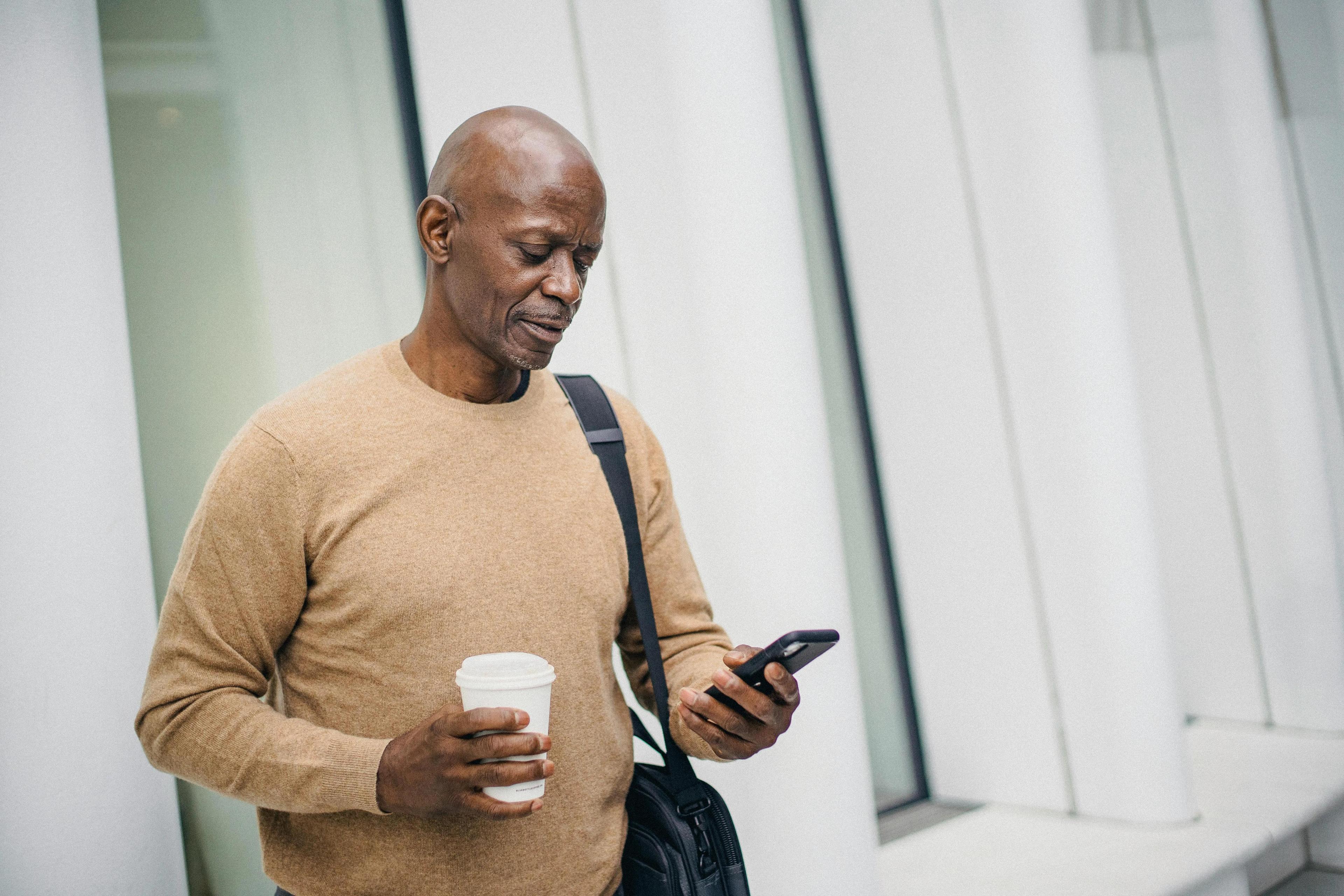 Man checking his phone while drinking coffee, illustrating the convenience of accessing marketing videos on the go.