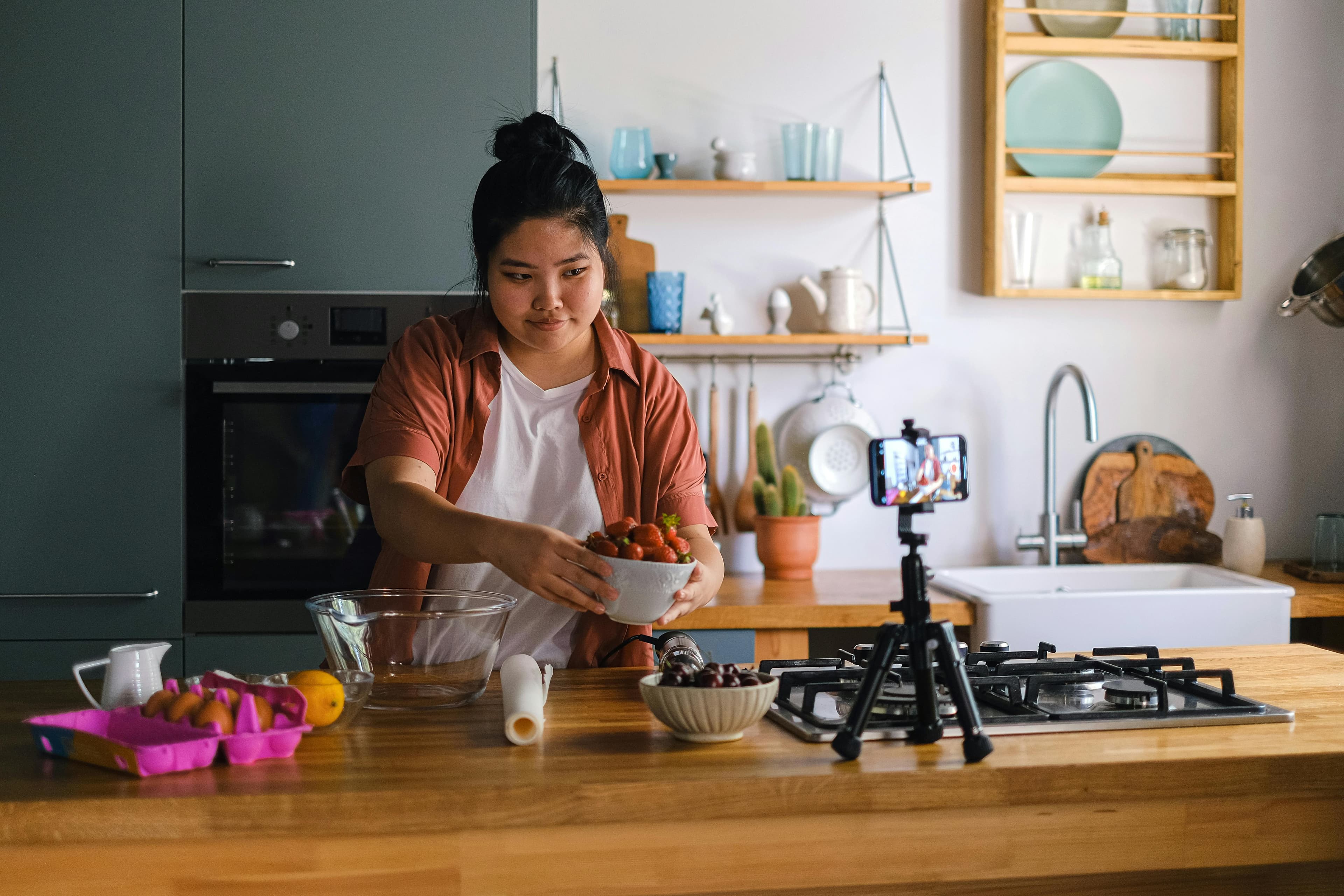 A content creator in a kitchen setting, preparing ingredients and recording with a smartphone on a tripod. This scene illustrates an engaging visual for "what is a lead magnet" in the context of cooking tutorials, where offering free recipes or video guides can attract potential subscribers.