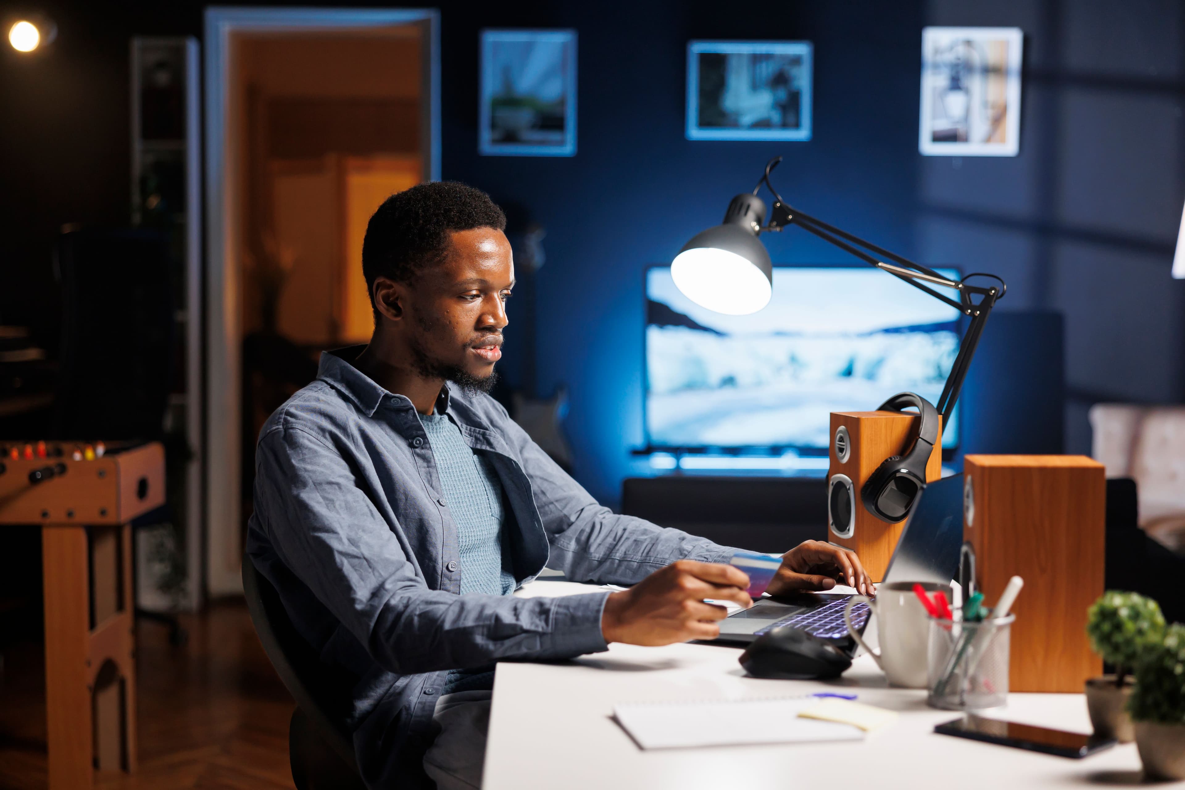 A man working on his computer in a cozy, modern room, focused on the screen with a dimly lit ambiance. This image represents "what is DTC marketing" by showing a direct-to-consumer business professional strategizing online marketing efforts to reach customers directly.