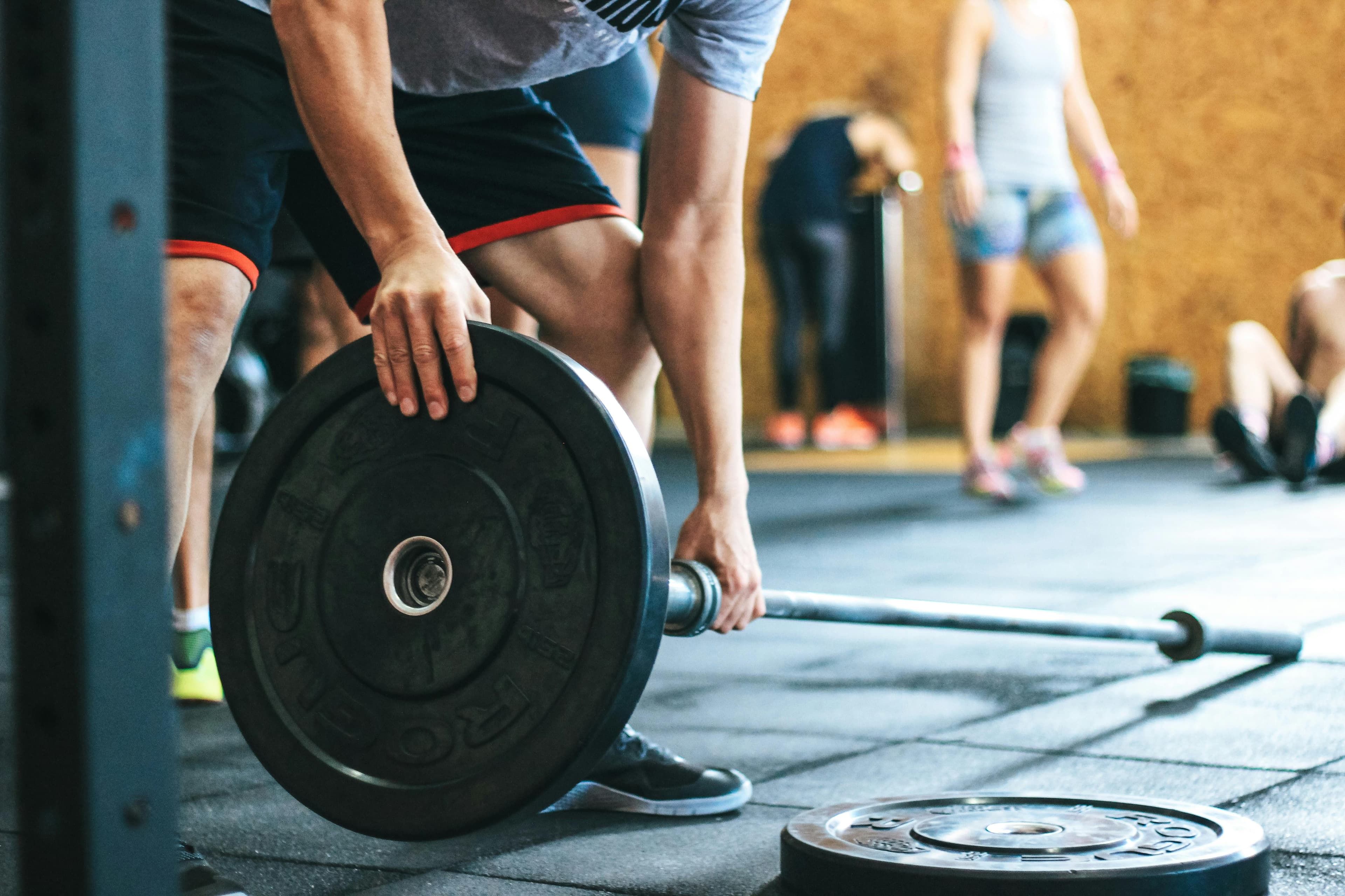 A person in a gym sets up a heavy barbell for weightlifting. This image can symbolize strength and determination, making it a great metaphor for building strong, high-converting websites with an AI landing page builder.